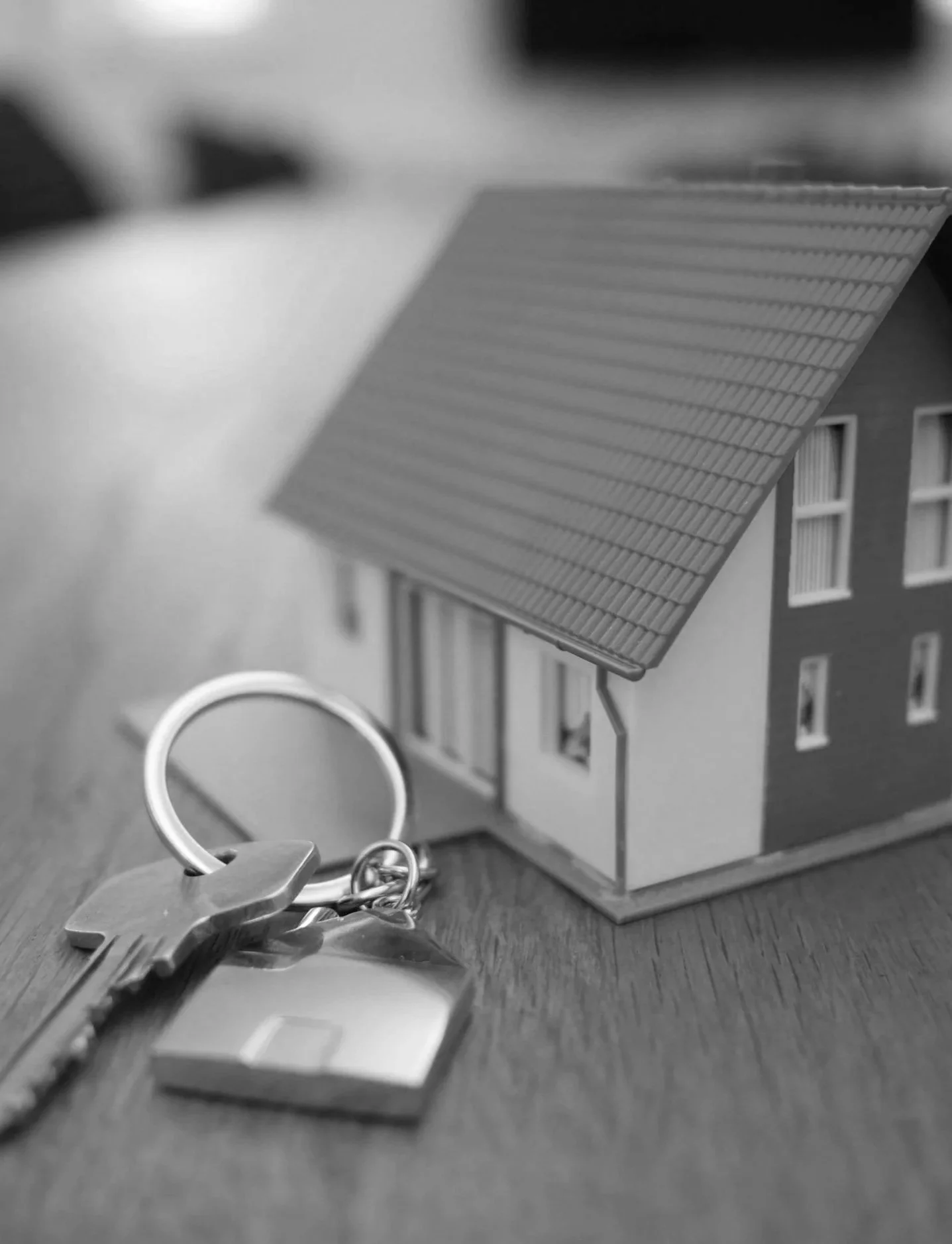 A small model house with a key and keychain on a wooden surface.