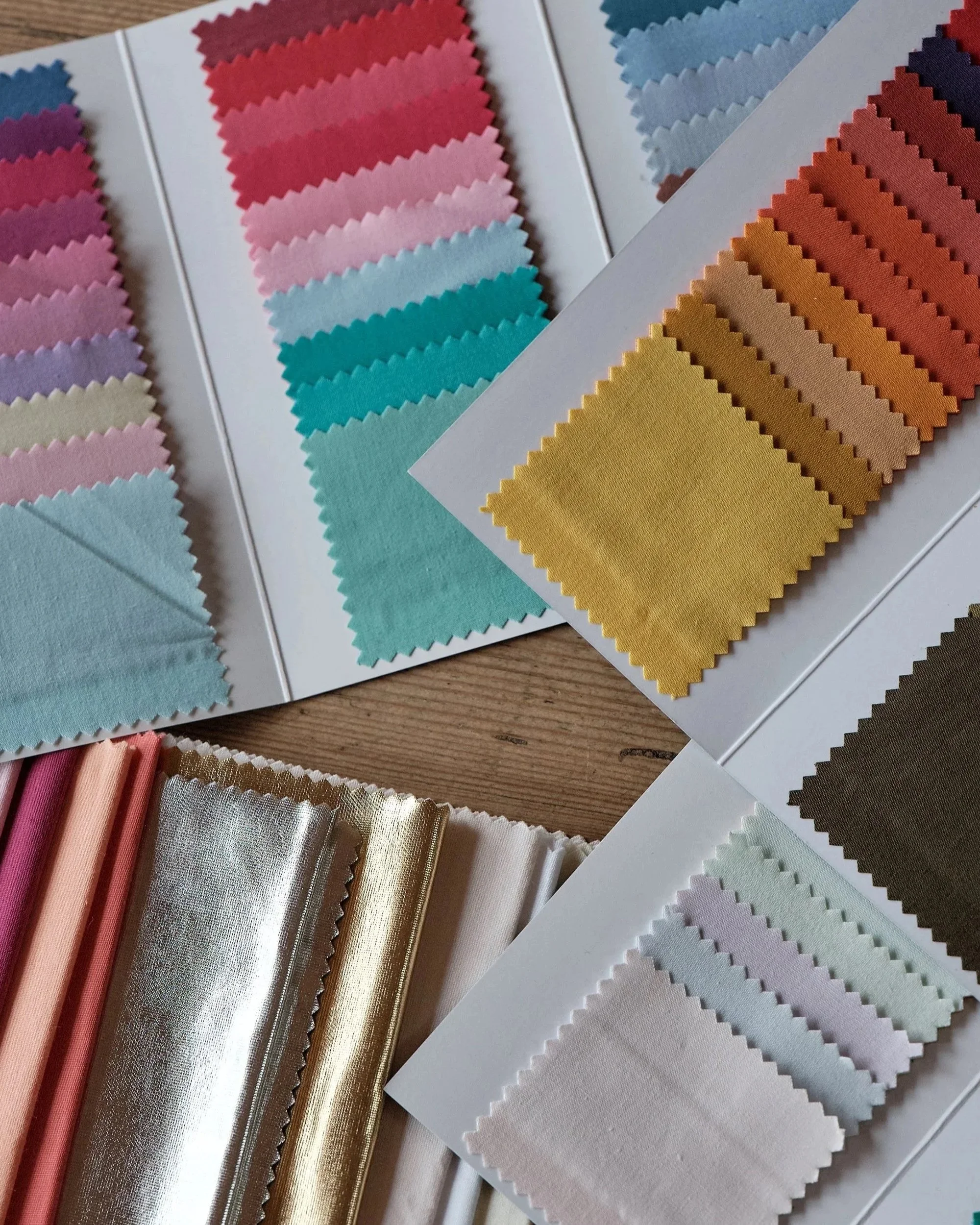 Swatches of fabric colour analysis drapes in various colours and textures arranged on white cards and a wooden surface.