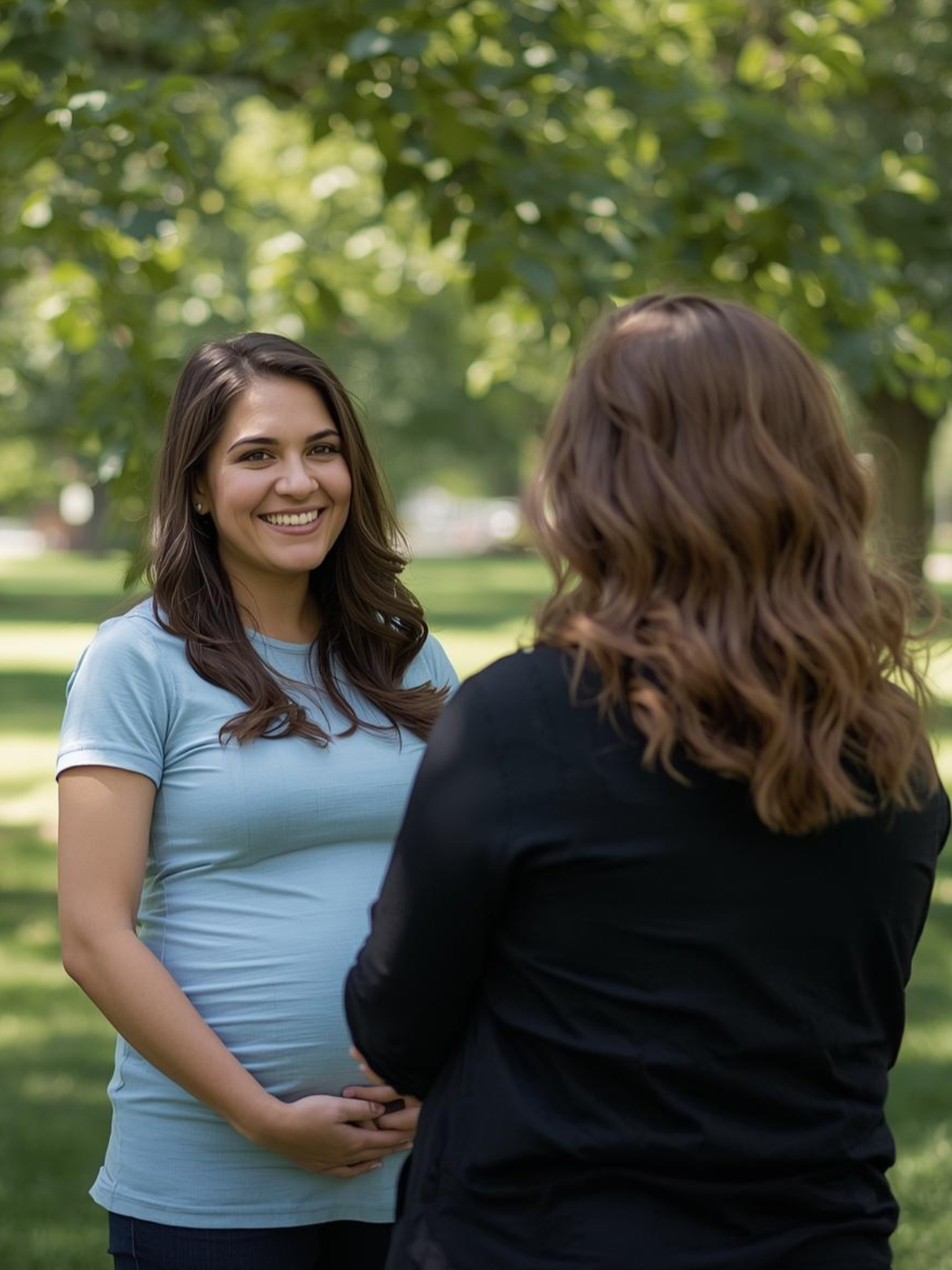 Une femme enceinte souriante parle avec une accompagnante périnatale dans un parc verdoyant.
