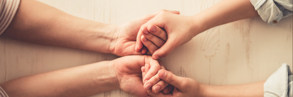 Deux mains tiennent une autre main dans une posture de soutien ou d'amitié sur une surface en bois clair.