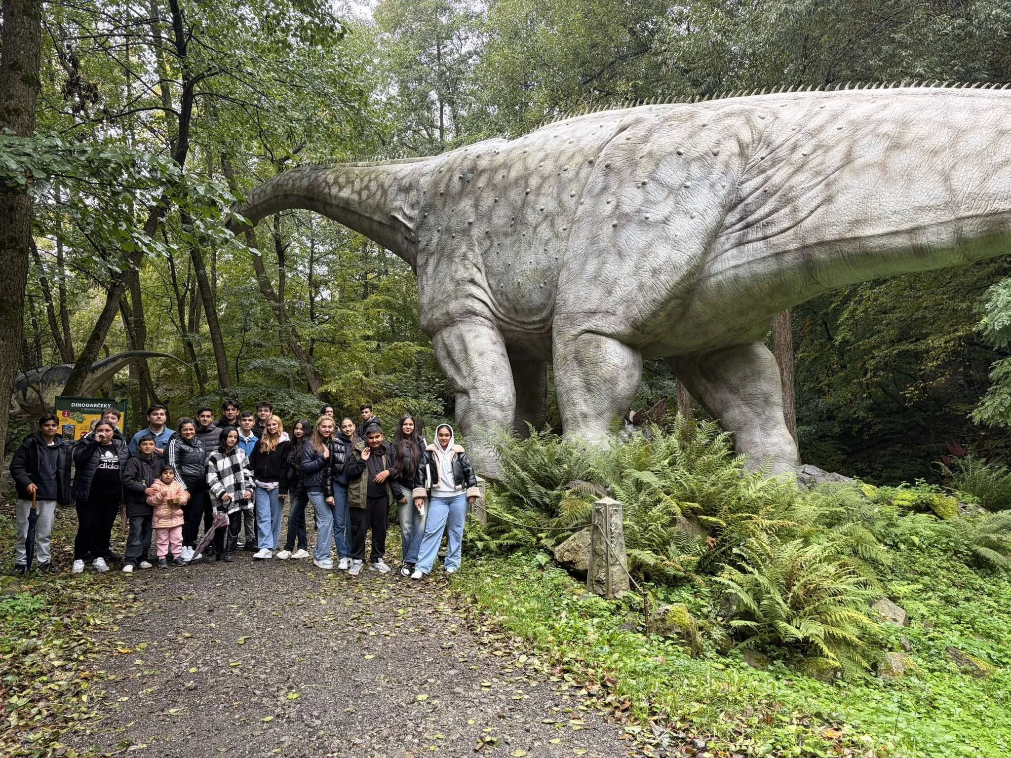 Group of people posing for a photo next to a large dinosaur statue in a forested area.