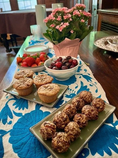 Table with strawberries, cherries, muffins, and energy bites, decorated with pink flowers.