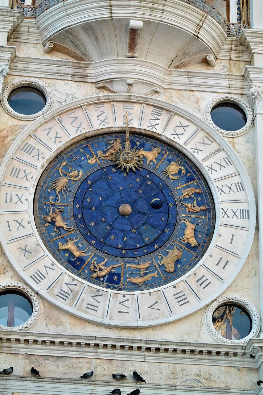 Clock with zodiac signs and Roman numerals on an ornate stone building.
