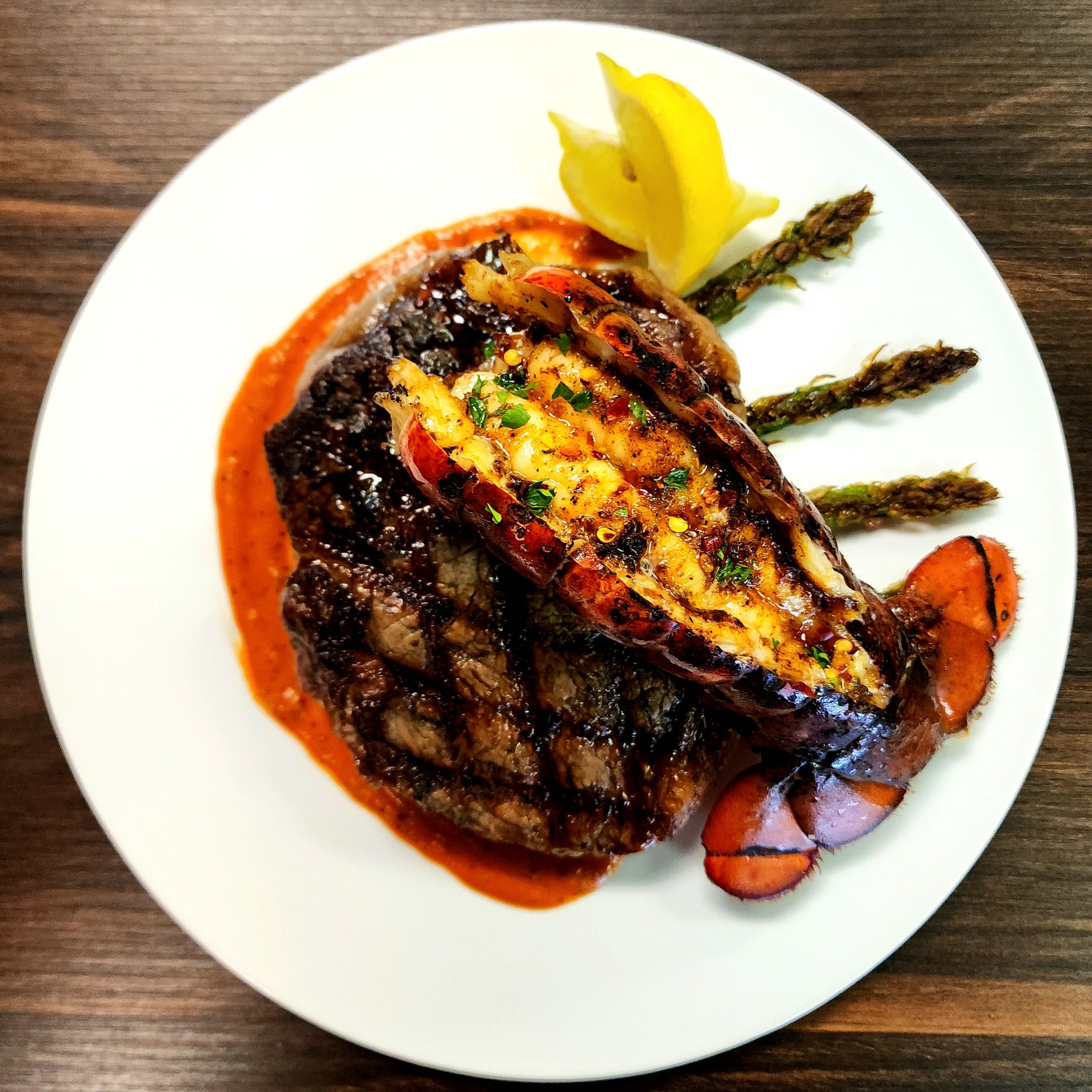 Lobster tail with grilled steak, asparagus, lemon wedge, and roasted carrots on a white plate