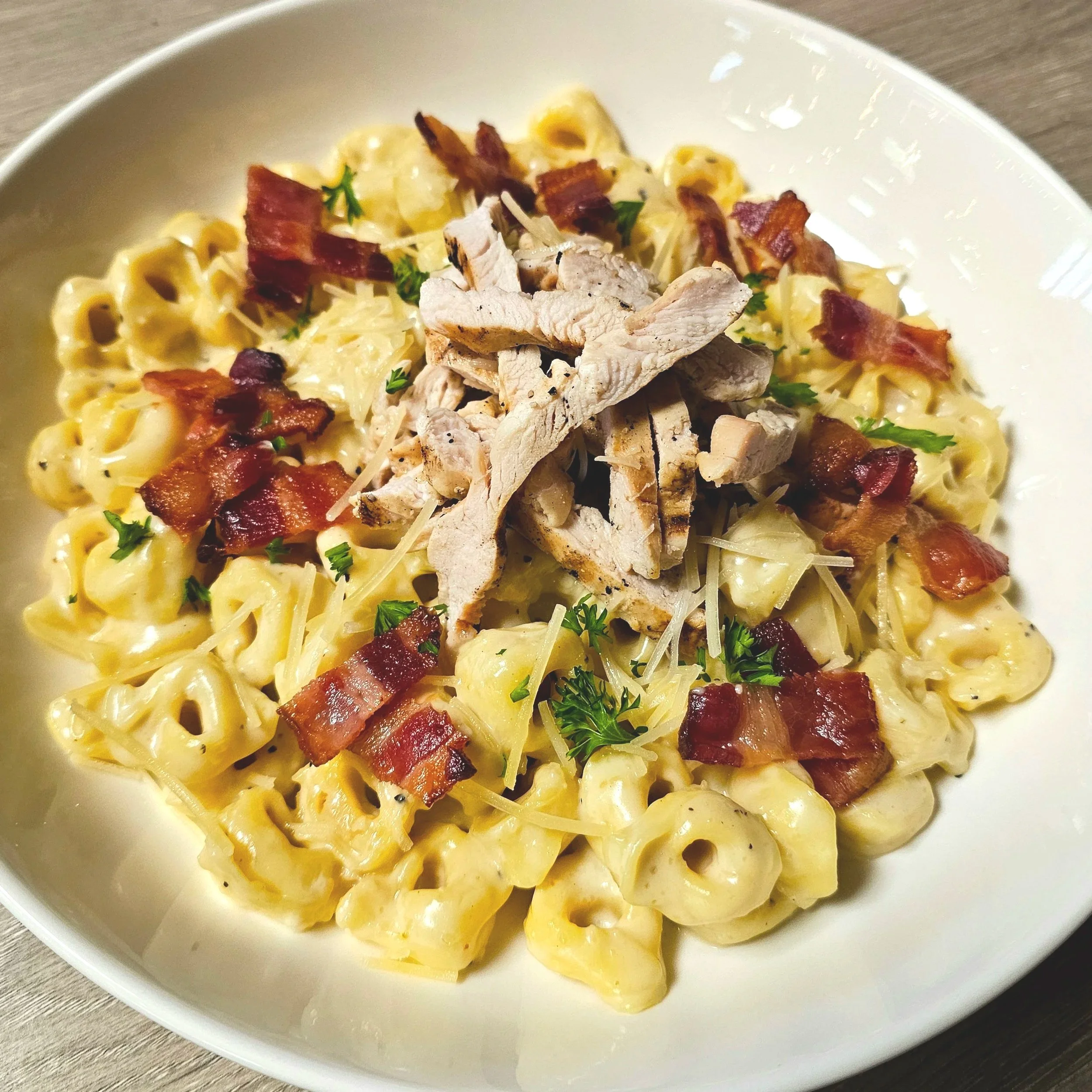 Bowl of macaroni and cheese topped with sliced grilled chicken, bacon bits, and parsley garnish.