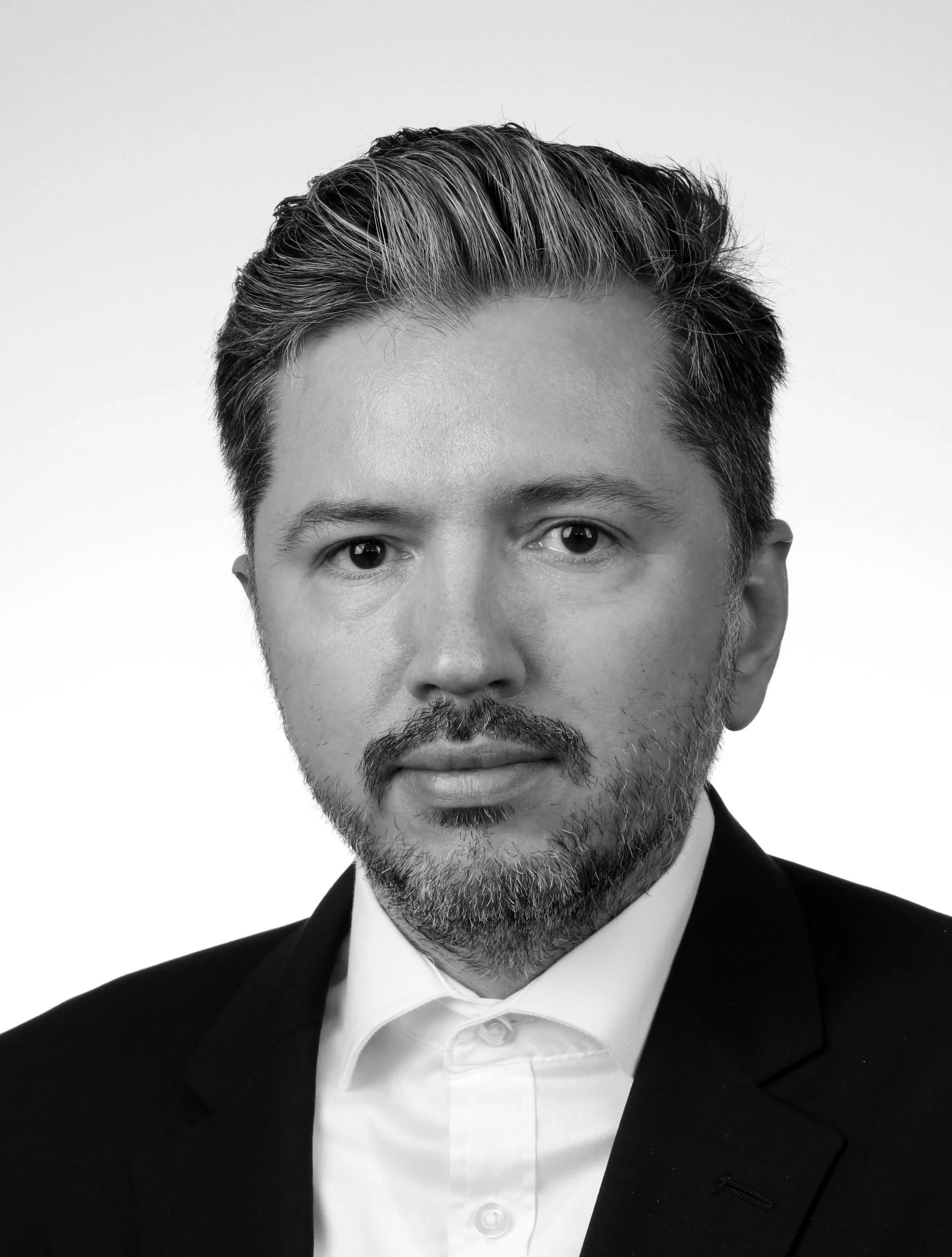 Black and white portrait of a man in a suit with a beard, looking directly at the camera.