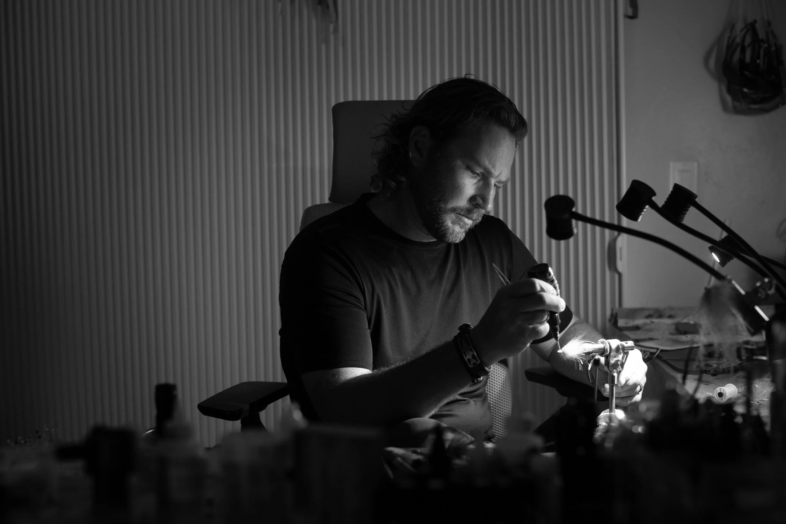 Drew Chicone tying flies at a workbench, using tools and vice, in a well-lit workshop.