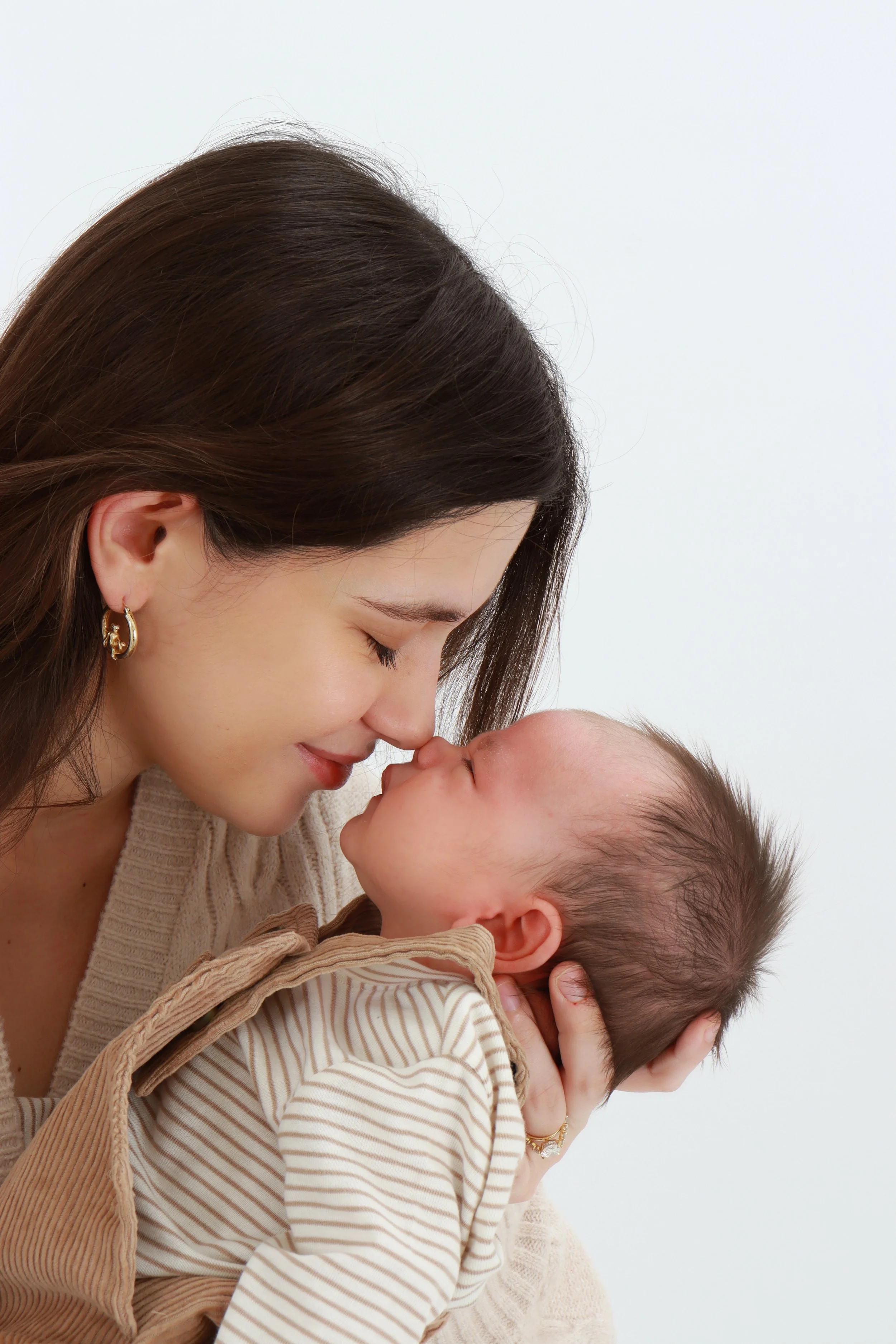 A woman holding a young child close, touching their noses together, both with closed eyes in an affectionate moment.