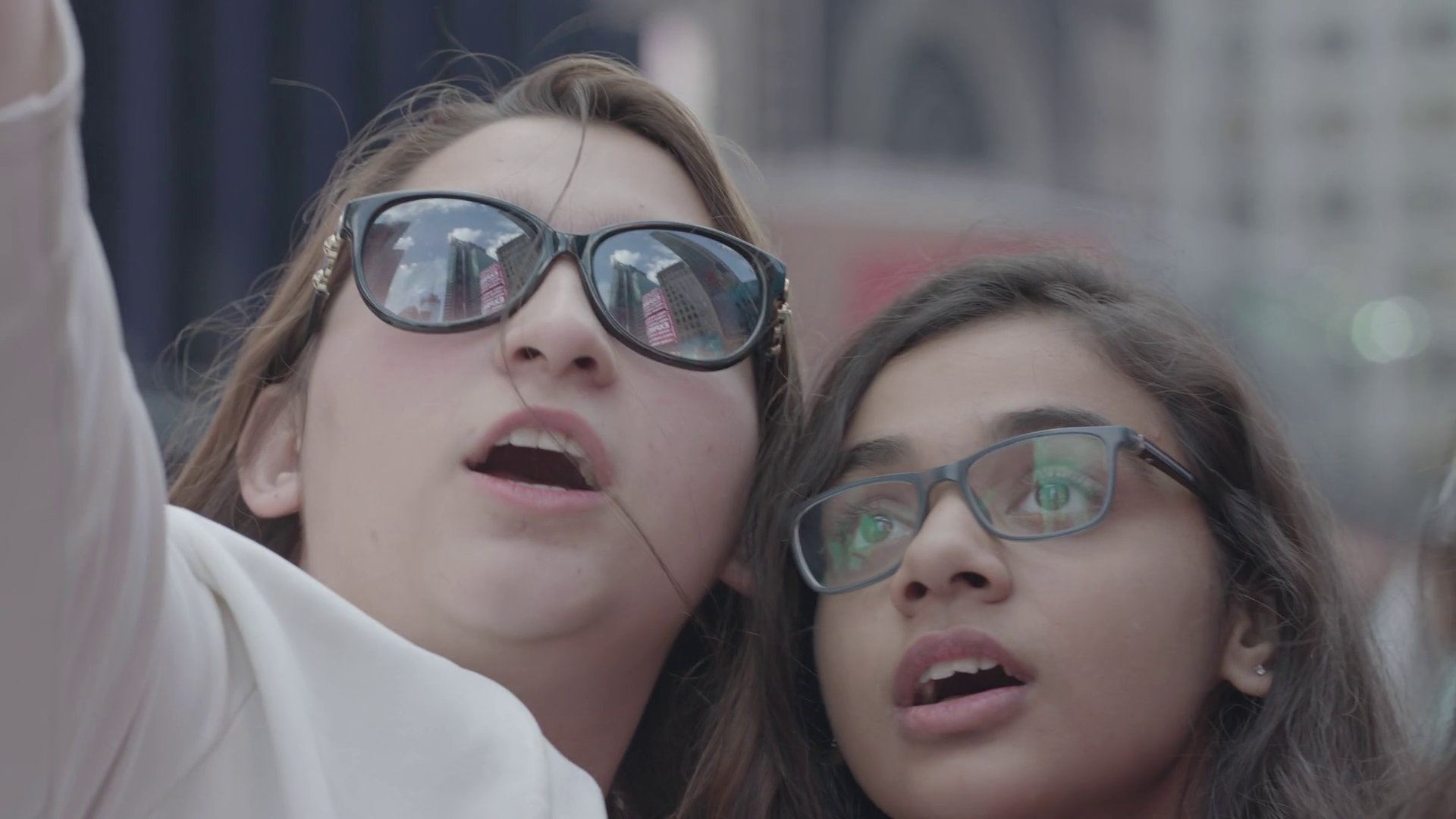 Two young women taking a selfie on a city street, wearing sunglasses and looking at the camera.