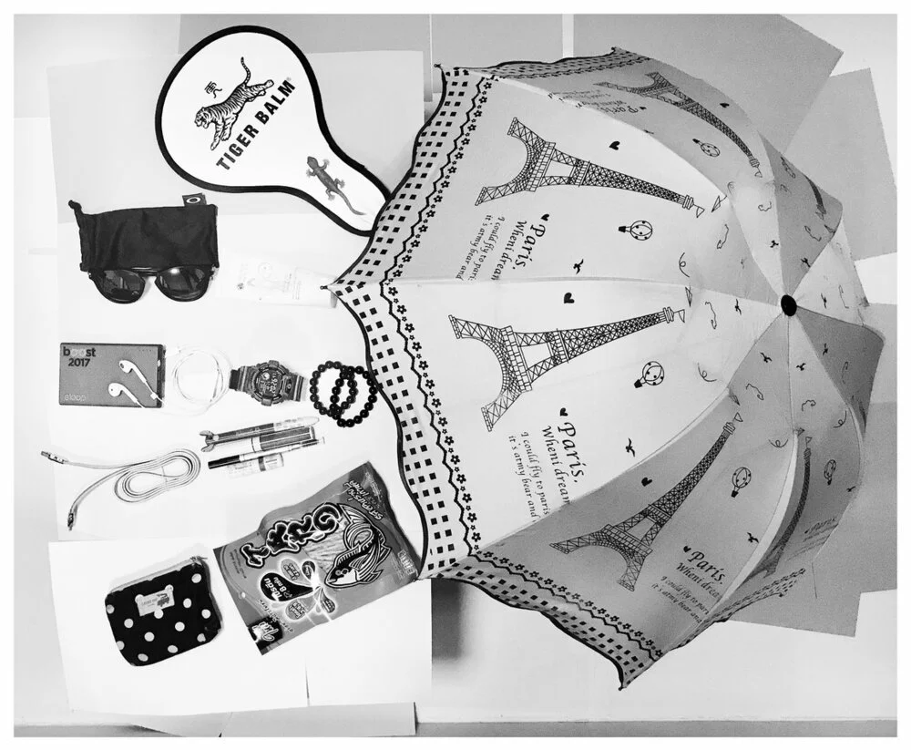 A collection of travel and everyday items arranged around a Paris-themed umbrella with illustrations of the Eiffel Tower.