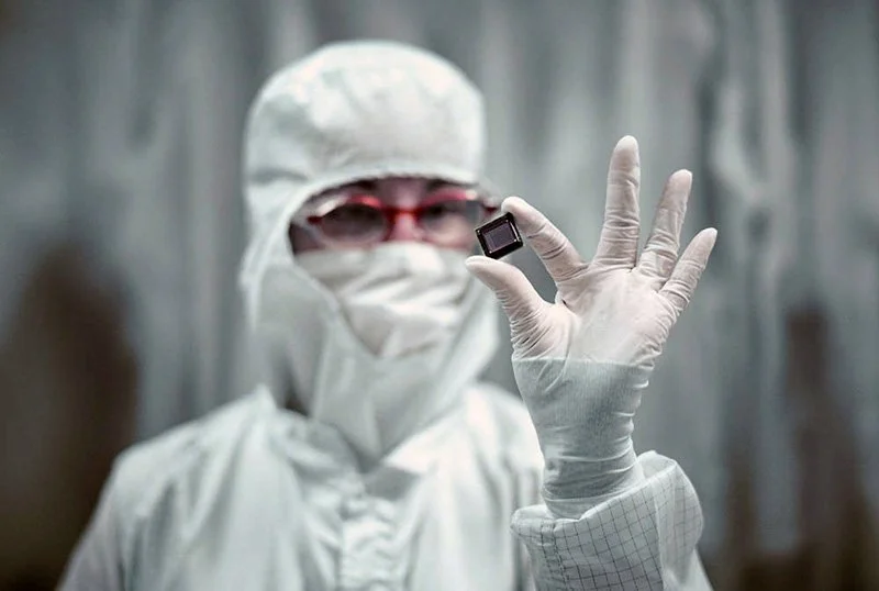Person in protective suit holding a small electronic chip