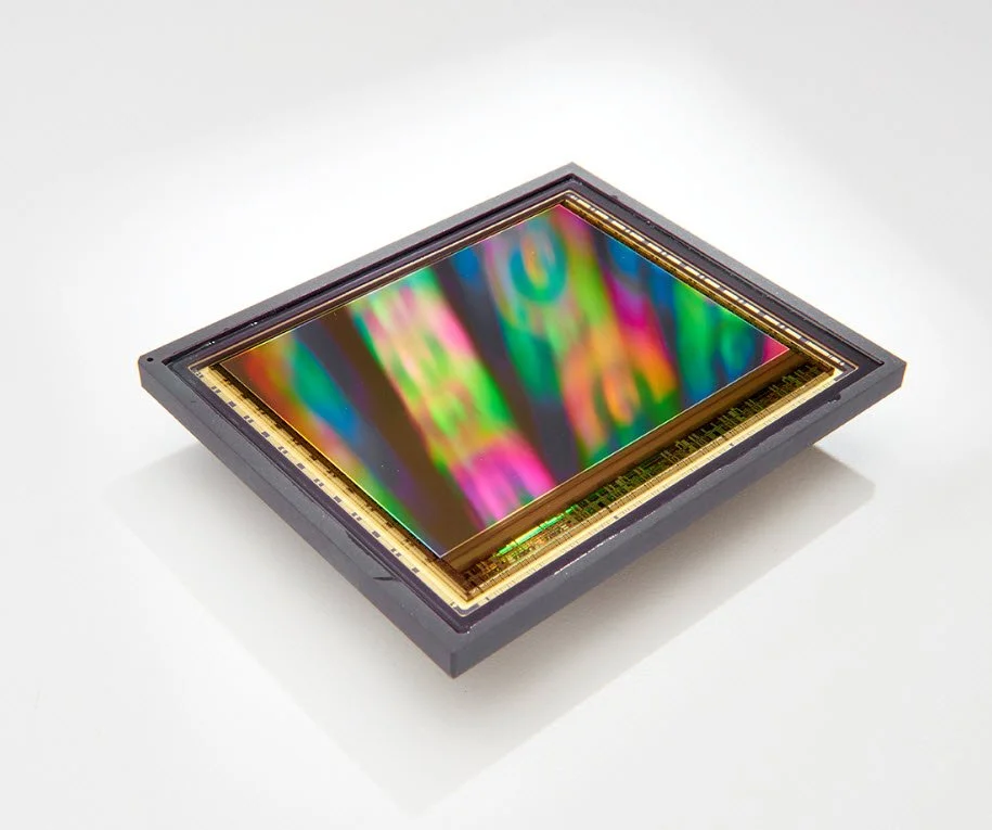 A microchip with a colorful reflective surface, resting on a white background.