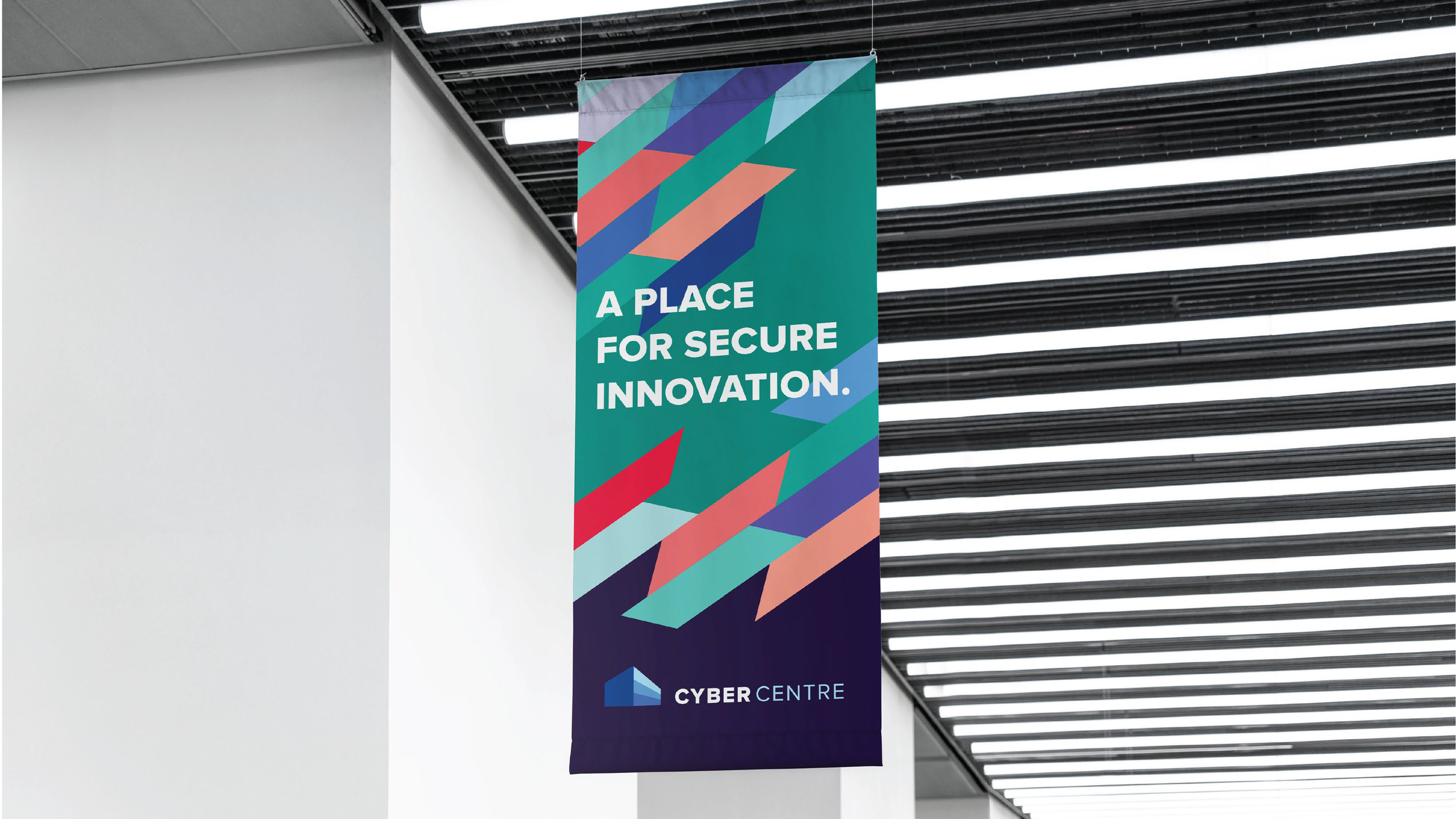 A vertical colorful banner with the text 'A PLACE FOR SECURE INNOVATION.' and the logo 'CYBER CENTRE' beneath, hanging from a ceiling in a modern building.