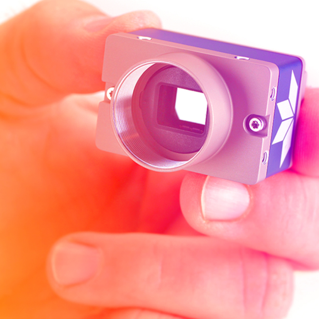 Close-up of a hand holding a small electronic device, specifically a camera without a lens, showing the sensor inside.
