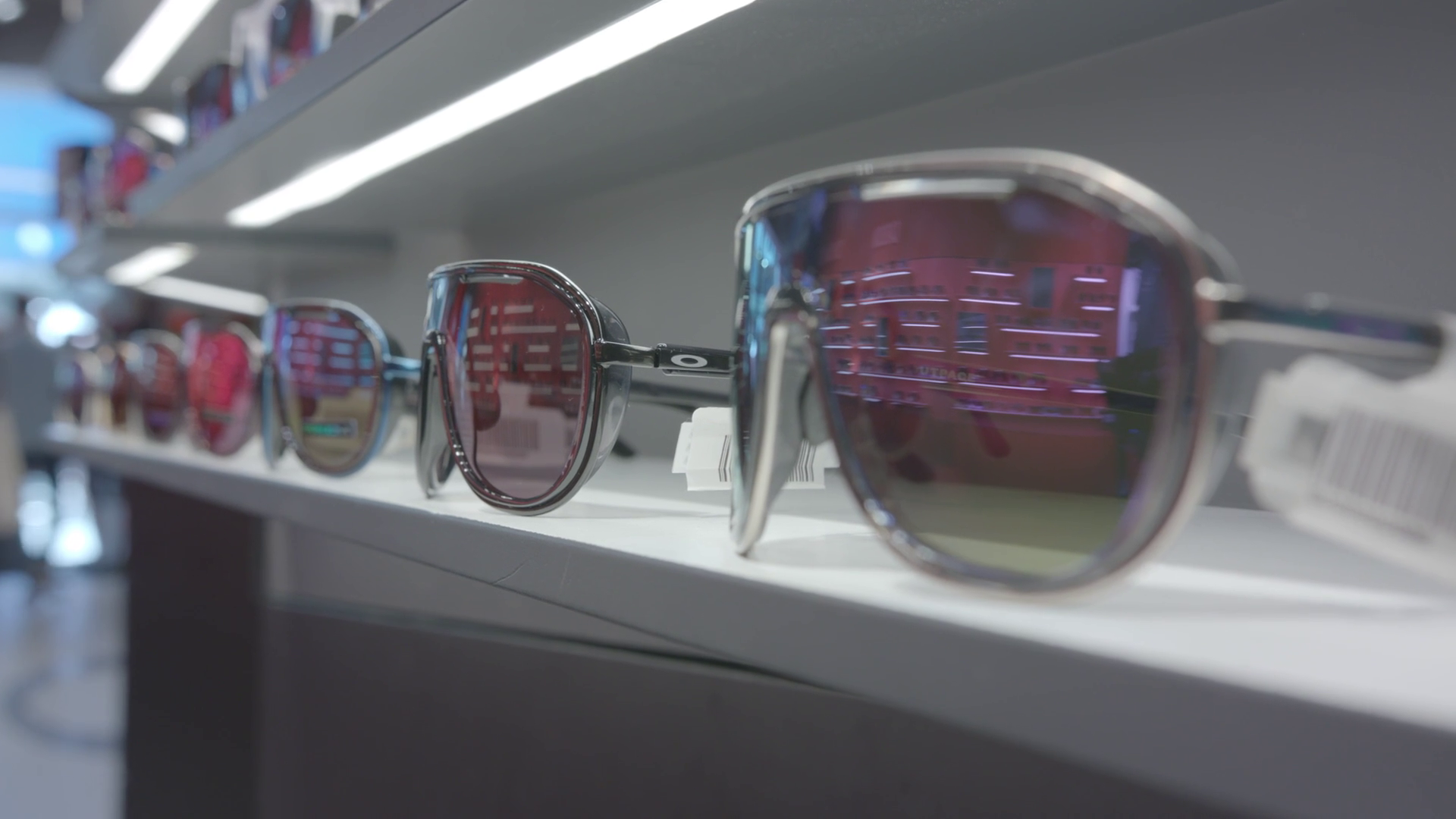 A row of sunglasses on a store shelf, with prominent sunglasses featuring reflective lenses in the foreground.