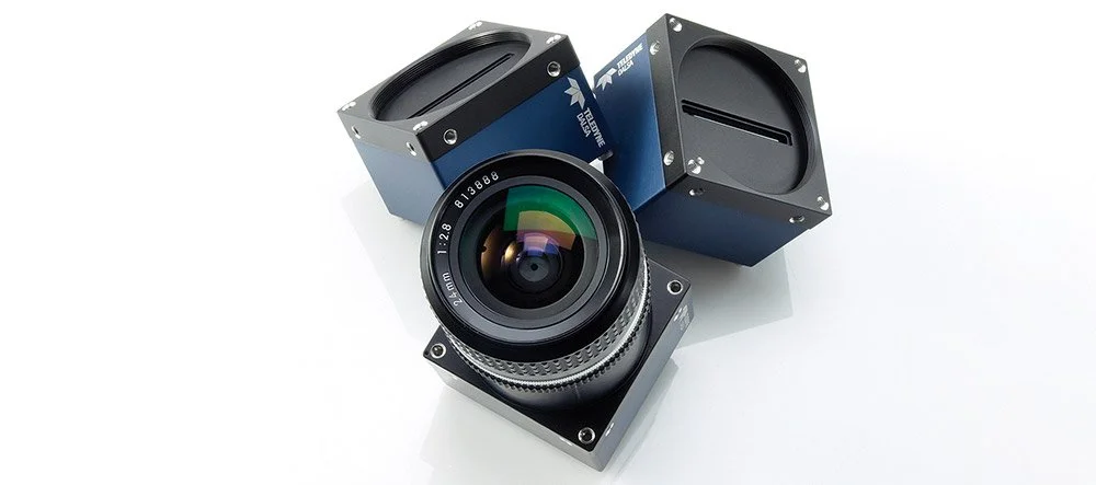 Three bluish cameras with black lenses, one larger than the others, on a white surface.