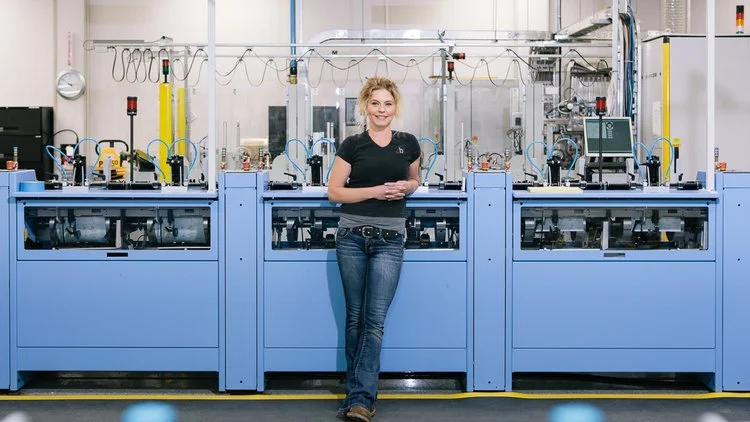 A woman standing in front of a large piece of industrial machinery in a laboratory or manufacturing setting.
