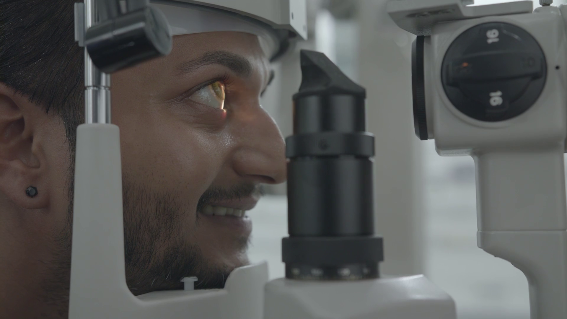 Close-up of a man at an eye examination, looking into a slit lamp device used by ophthalmologists.