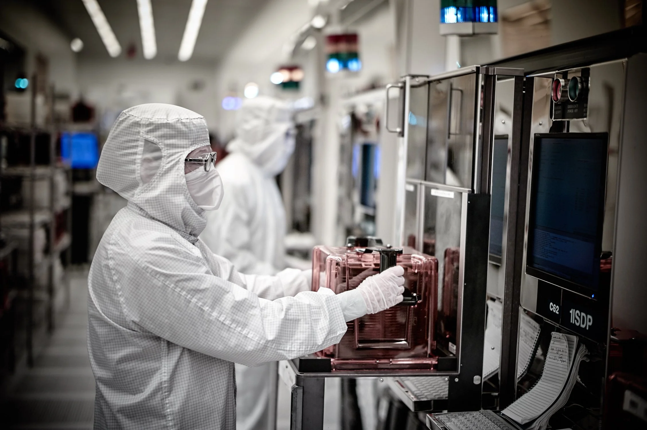 Workers in cleanroom suits operating laboratory equipment in a pharmaceutical manufacturing facility.