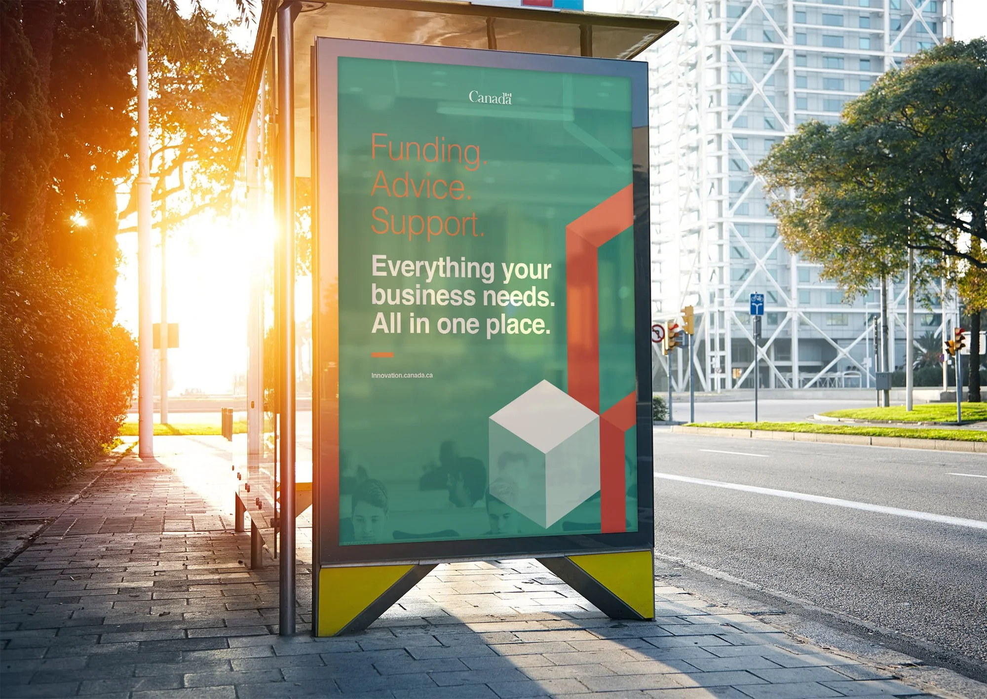 An advertising billboard on a sidewalk next to a street, featuring a green background with text promoting business services, with the sun setting in the background and city buildings in the distance.