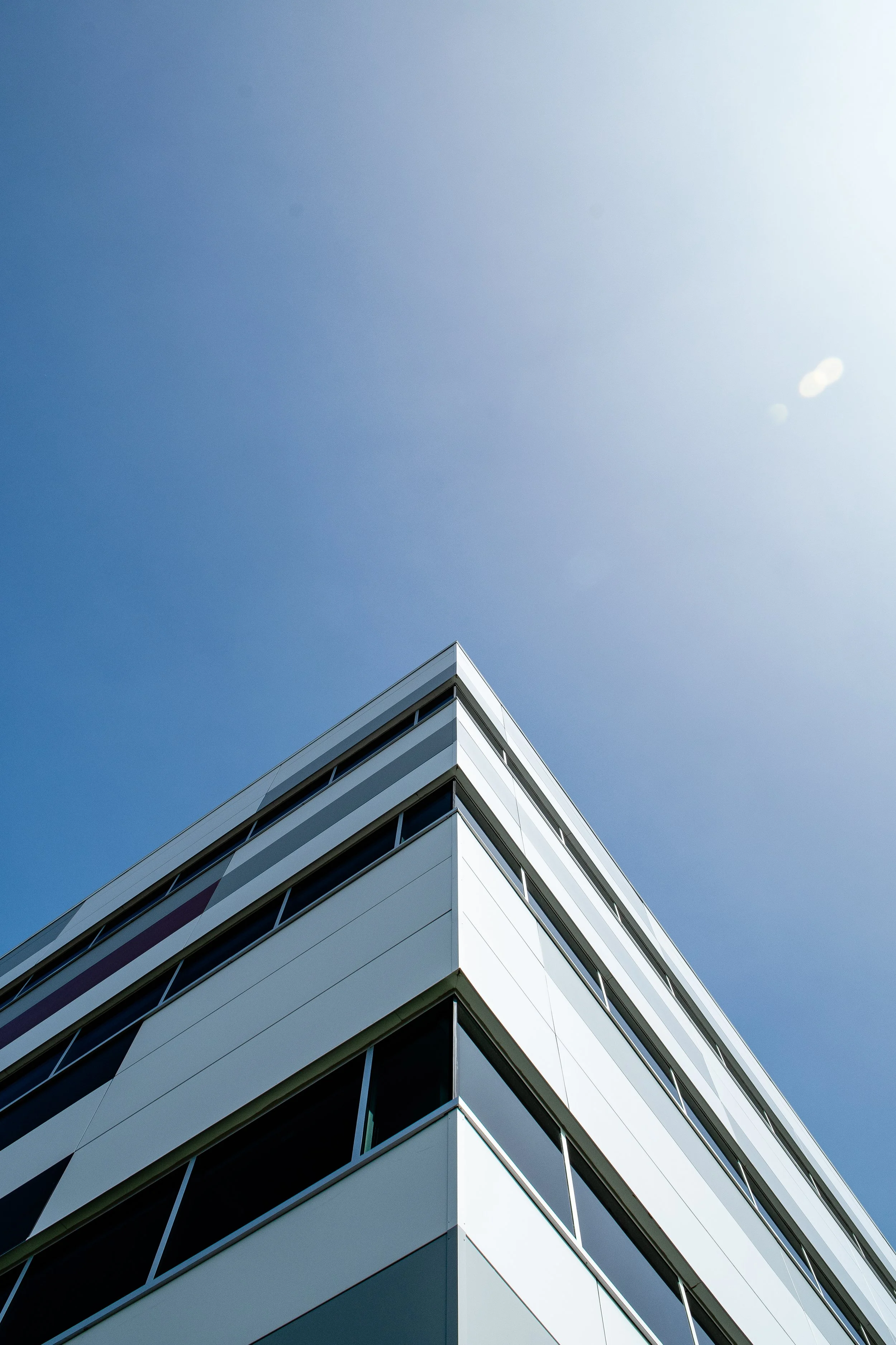 Low-angle view of a modern white apartment building against a clear blue sky.