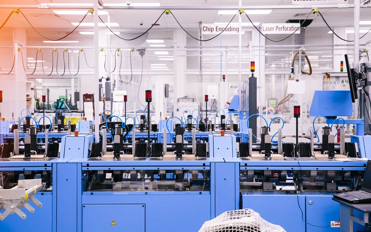 A high-tech manufacturing laboratory with blue machinery, wiring, and equipment for chip encoding and laser perforation.