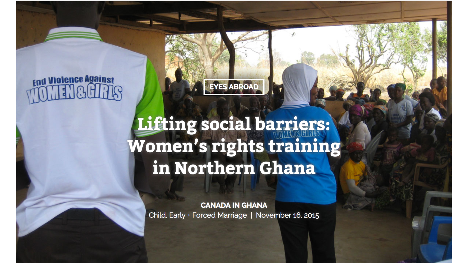 Women and girls attending a social training session in a rural building in Northern Ghana, with two women wearing blue shirts with 'Women & Girls' slogan on the back, and a crowd of seated women in the background.