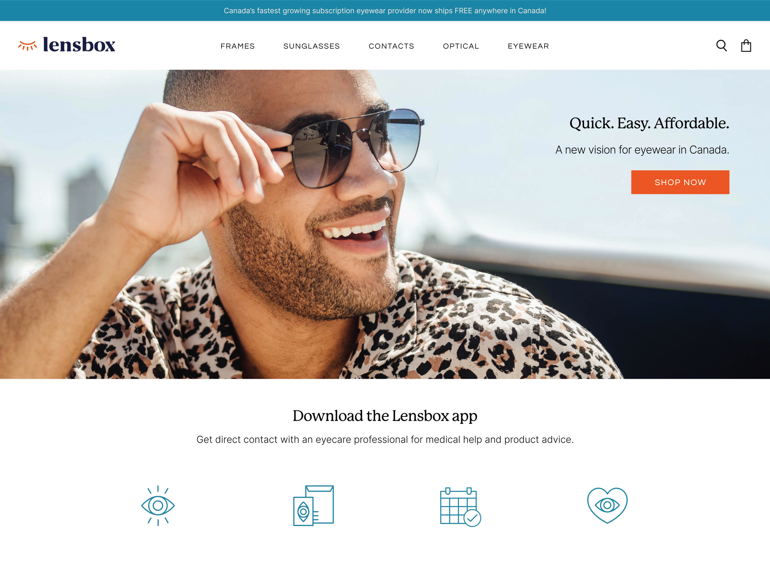 A man smiling while wearing sunglasses, sitting outdoors with a blurry cityscape background, wearing a leopard print shirt.