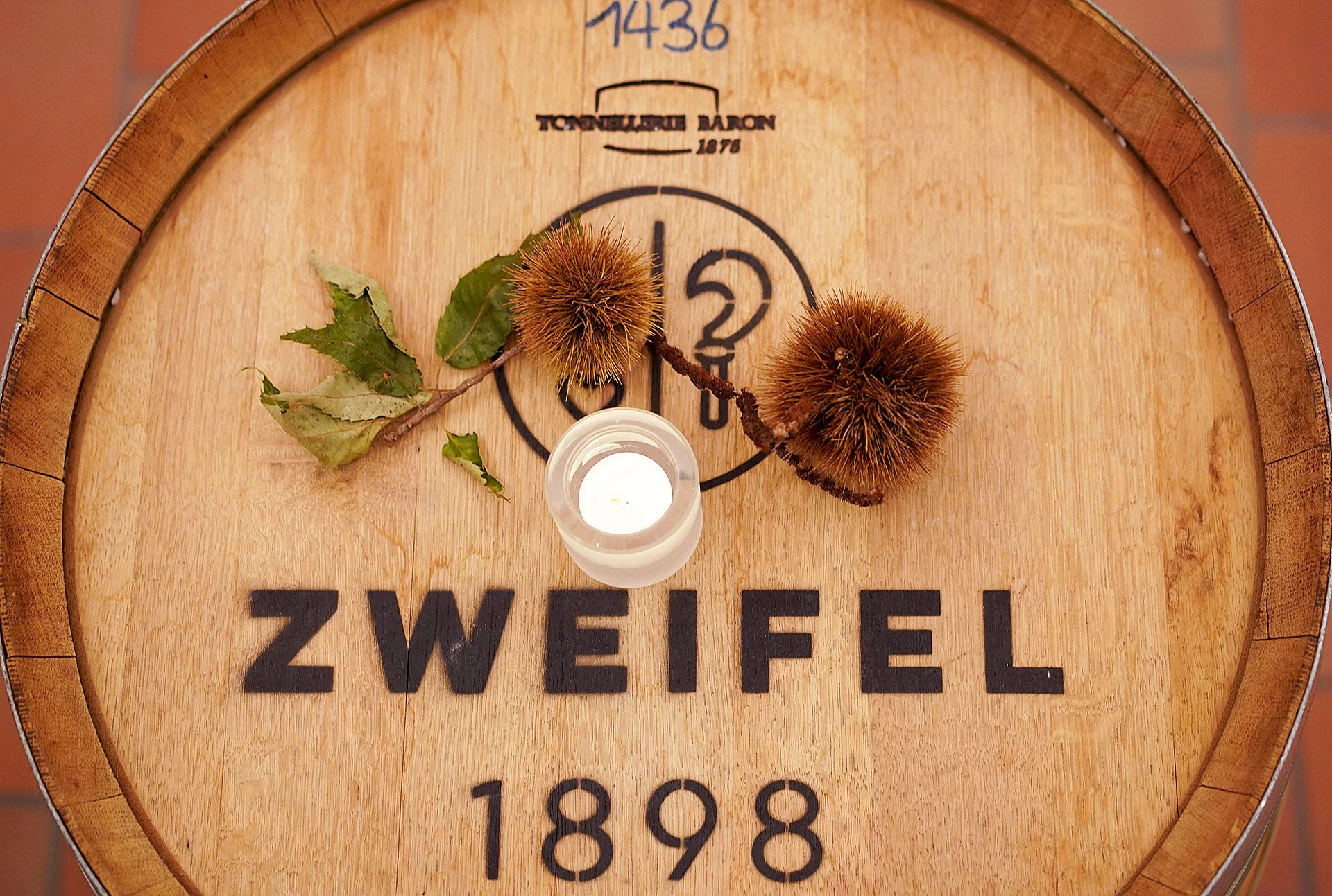 Holzfass mit Schriftzug, festlich dekoriert mit Blättern und ein Kerzenglas auf dem Fassboden