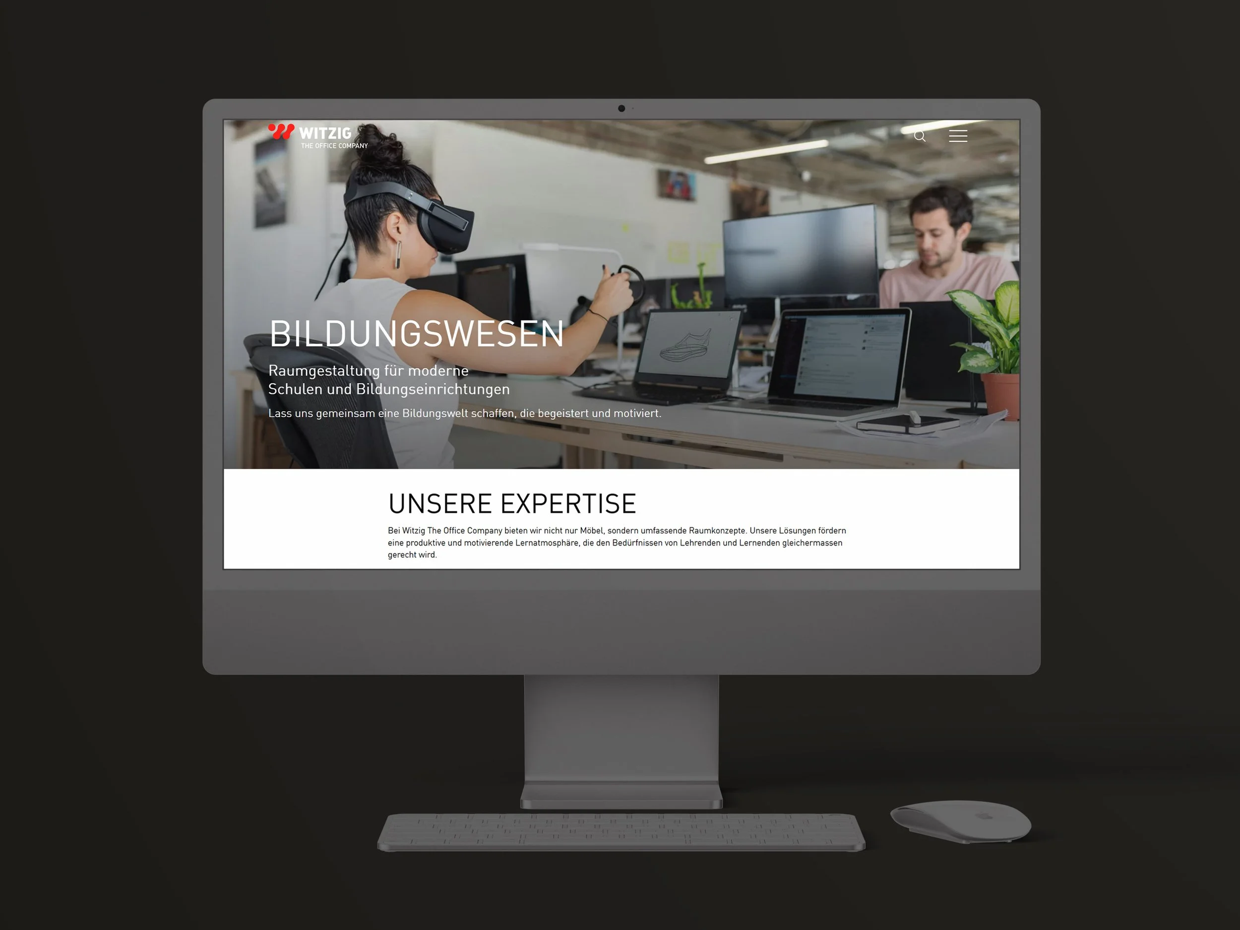 Bildschirm mit Website von Witzig The Office Company, zeigt eine Frau mit Virtual-Reality-Brille am Arbeitsplatz, umgeben von Laptops und einem Mann bei der Arbeit.