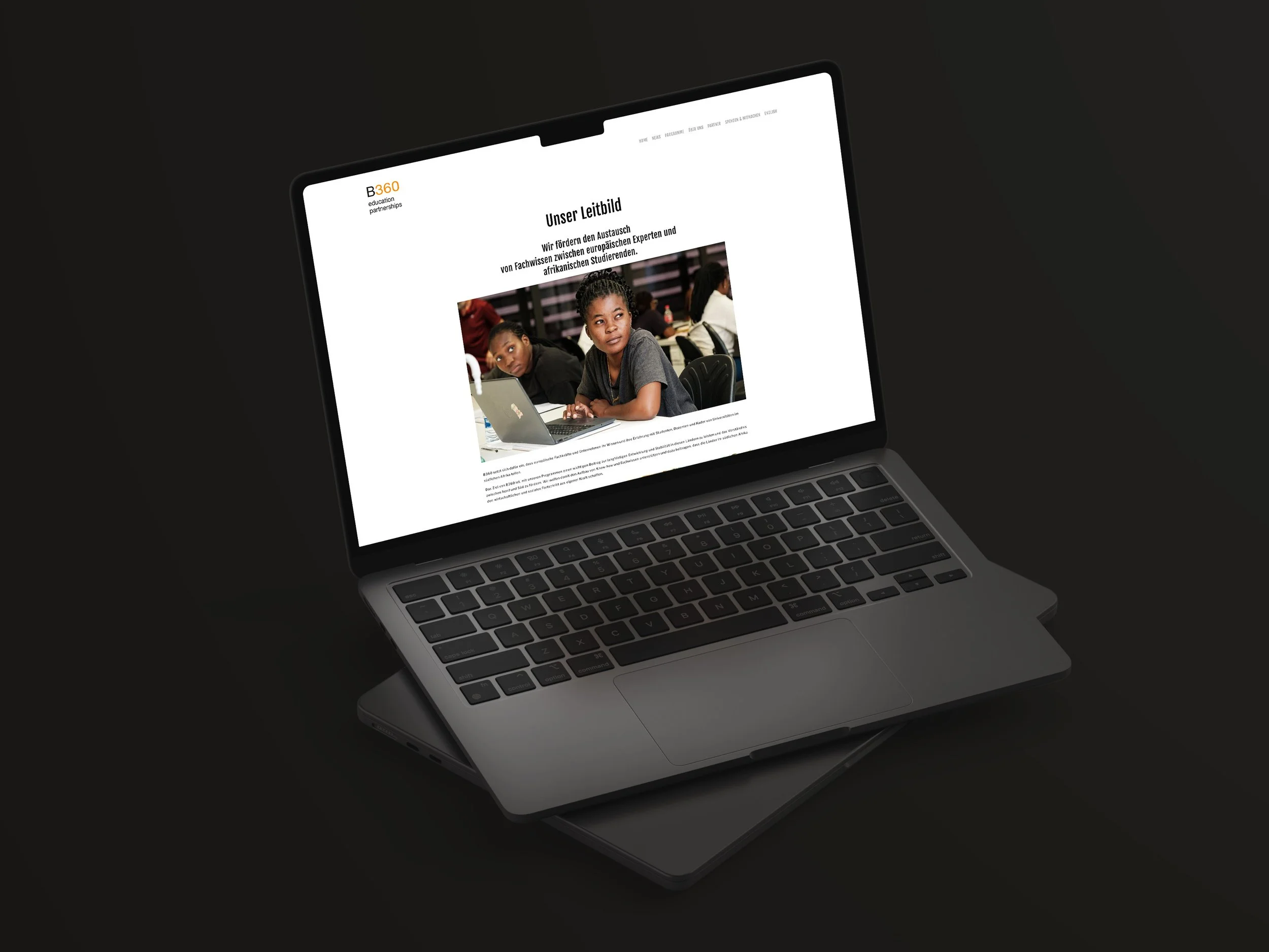 Laptop mit einer Webseite auf Deutsch, die den Titel "Unser Leitbild" trägt. Es zeigt ein Bild von Kindern, die in einem Klassenraum sitzen.
