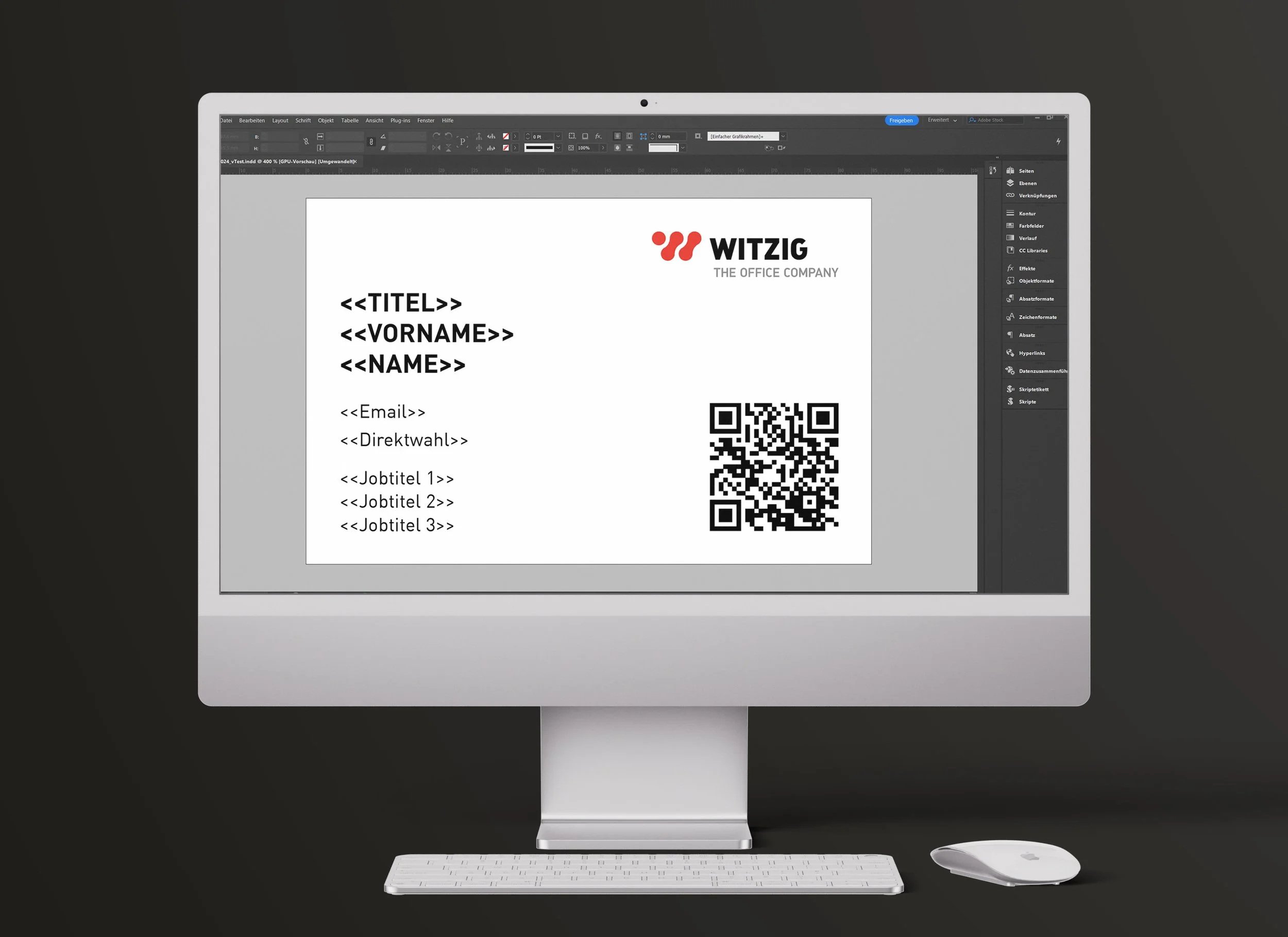 Ein Apple iMac-Computer mit einer Tastatur und einer Maus auf einem schwarzen Hintergrund, auf dem Bildschirm läuft eine Grafikdesign-Software mit der Vorlage einer Visitenkarte.