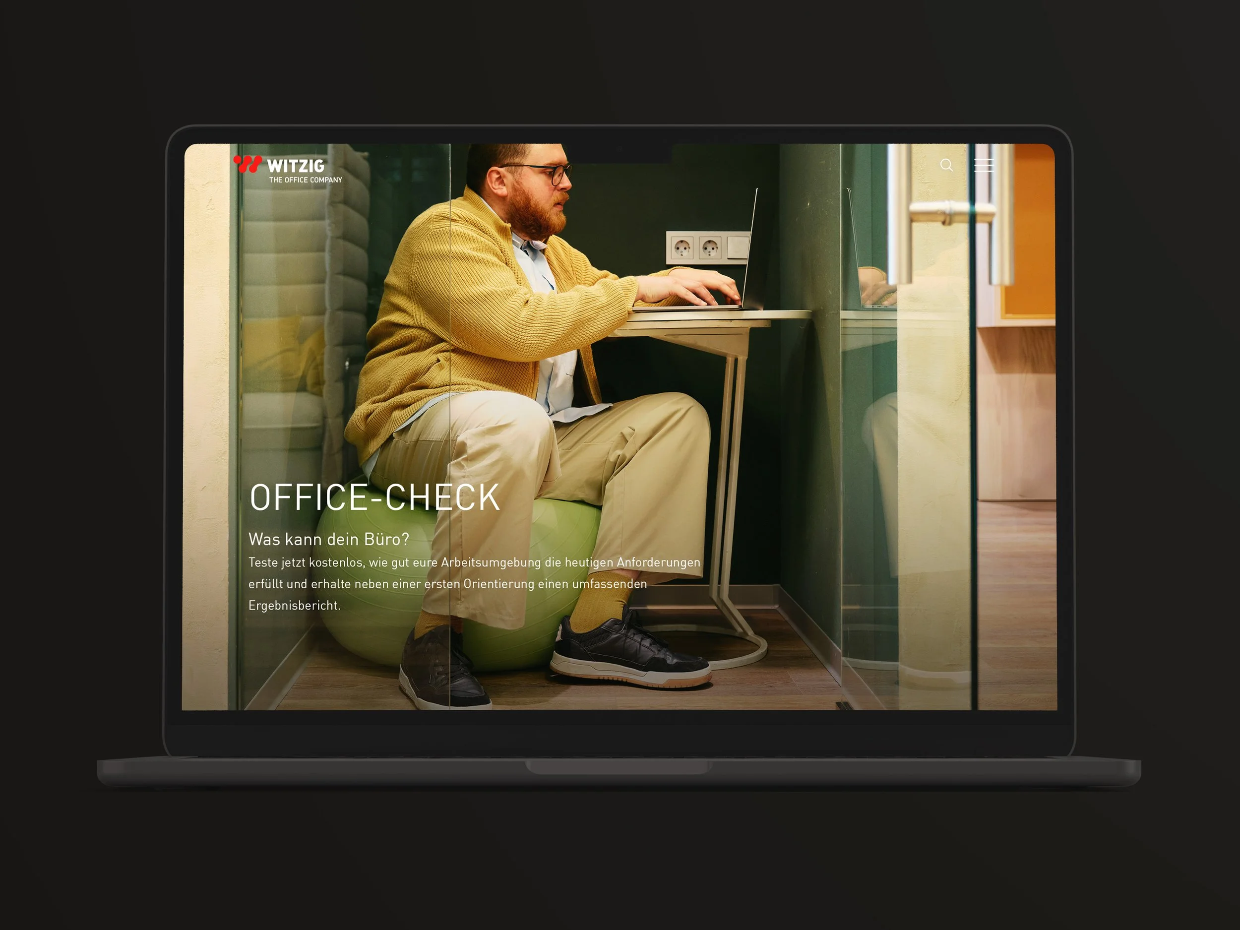 Ein Mann mit Brille, gelber Strickjacke und beige Hosen sitzt in einem kleinen, leeren Büroraum mit grüner Wand und einer elektrischen Steckdose hinter ihm, während er auf einen Laptop schaut. Der Raum ist in einer Multimedia-Anzeige mit dem Text "Office-Check" und einer kurzen Beschreibung eingebettet.