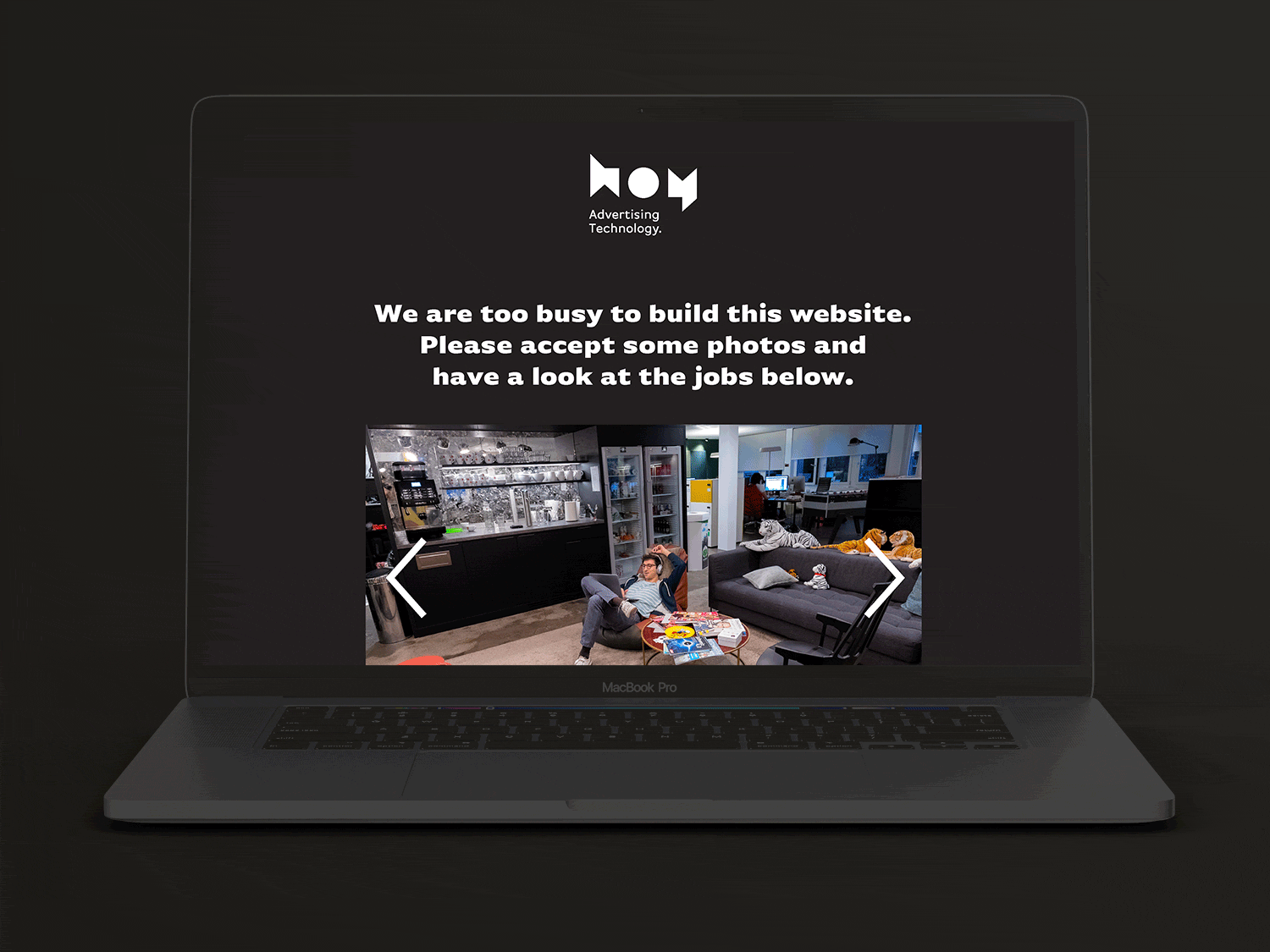 Bildschirm zeigt eine Webseite mit einem schwarzen Hintergrund, einem weißen Logo, Text in der Mitte und einem Foto von einem gemütlichen Raum mit Personen, die auf Sofas sitzen und an Laptops arbeiten.
