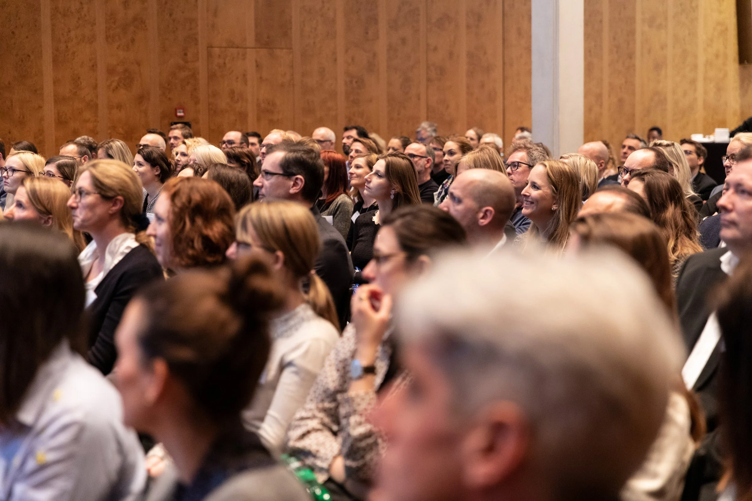 Menschen sitzen in einem großen Saal bei einer Konferenz oder einem Vortrag, die Atmosphäre ist aufmerksam und interessiert.