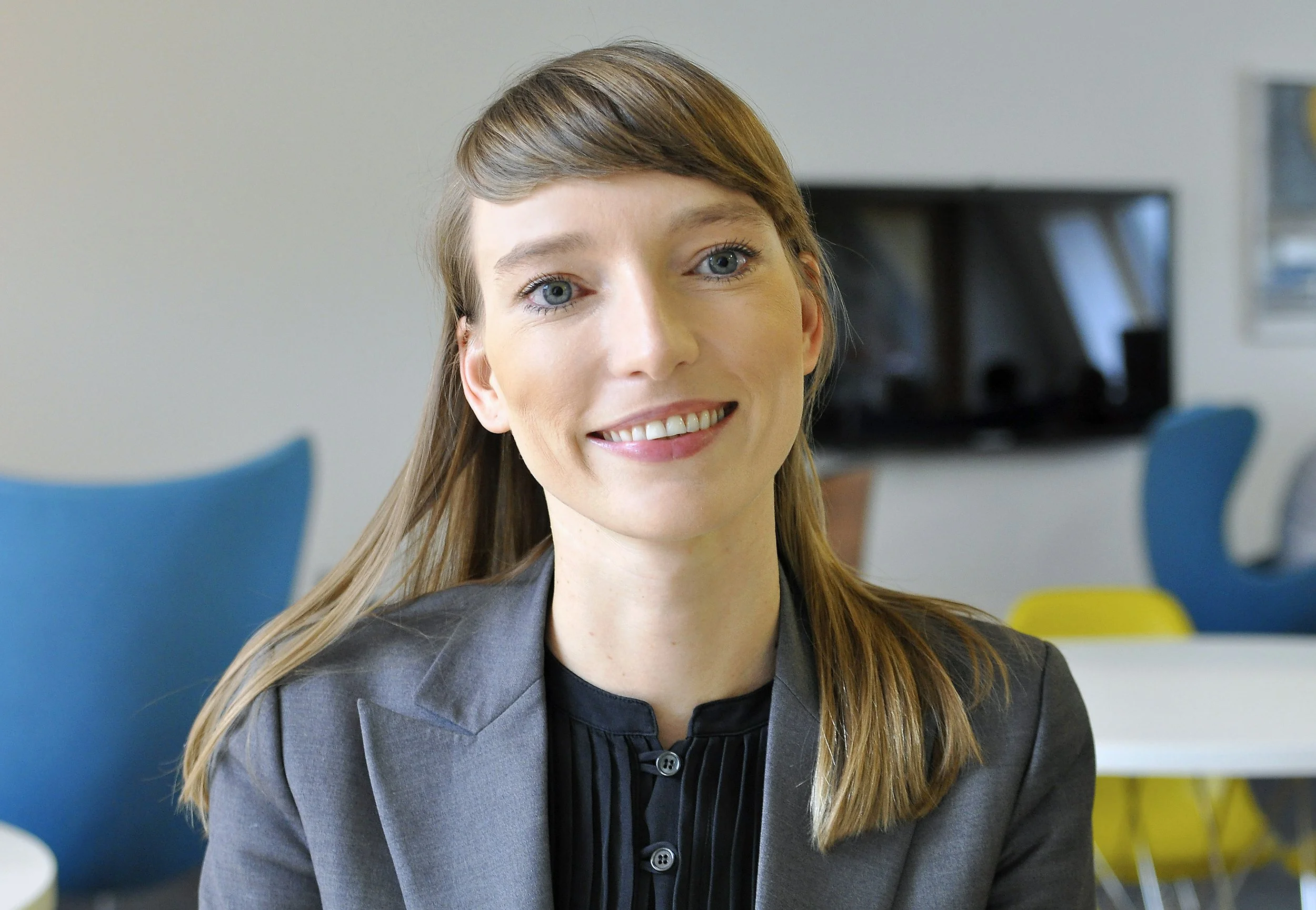 Porträt einer lächelnden Frau mit blonden Haaren im Business-Outfit in einem modernen Büro.