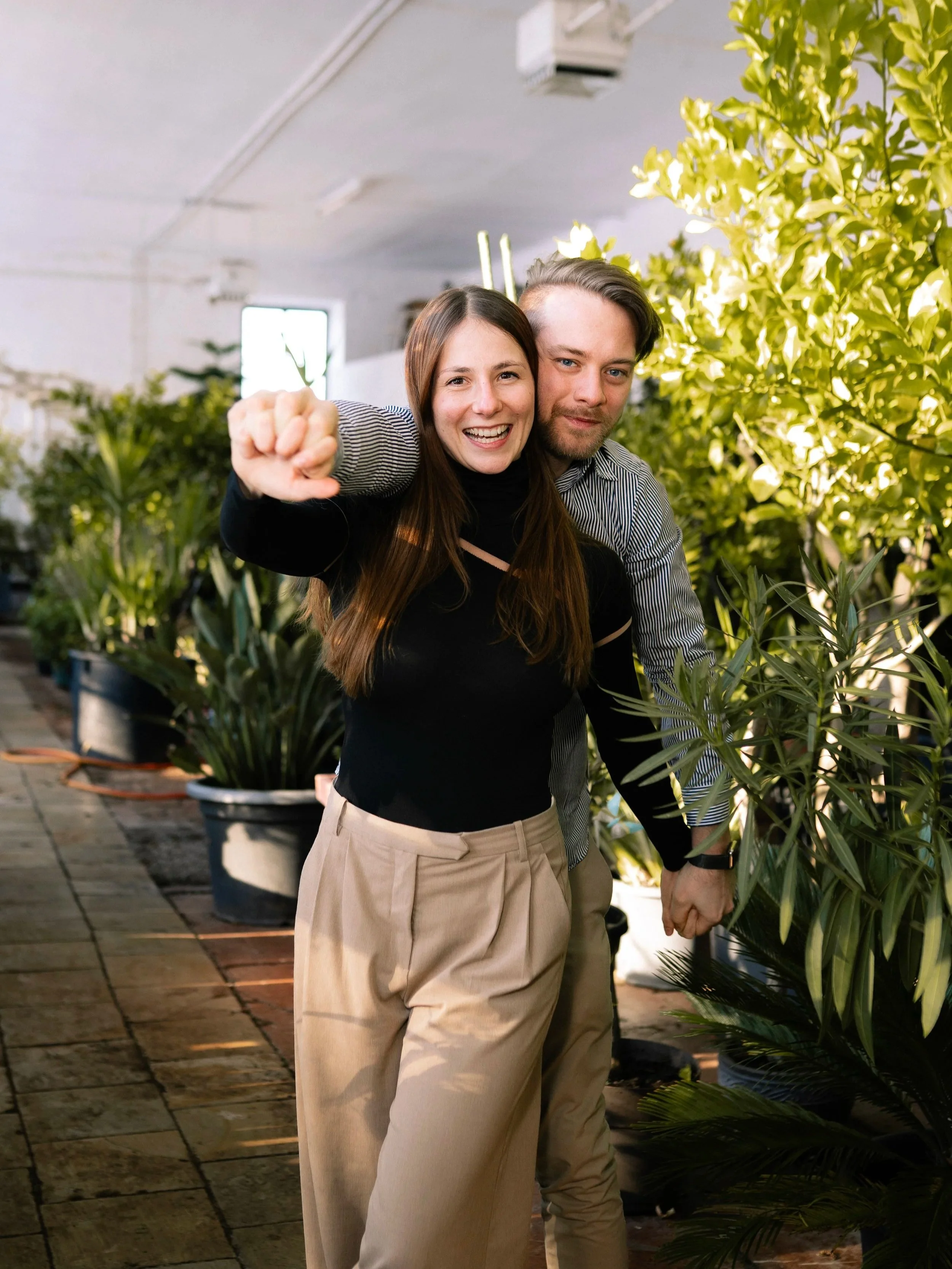 Ein lachendes Paar, die Frau zeigt einen Daumen nach oben, ist in einem Raum mit vielen Pflanzen.