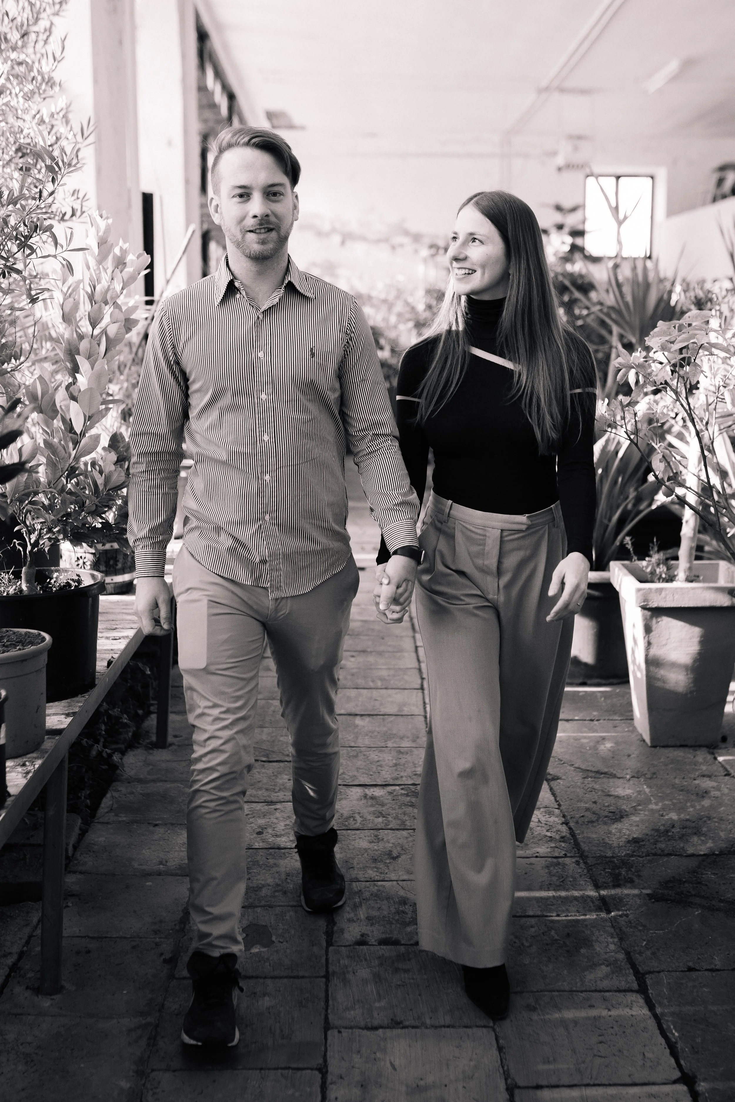 Ein Mann und eine Frau halten Händchen beim Spaziergang durch ein Gewächshaus mit Pflanzen.