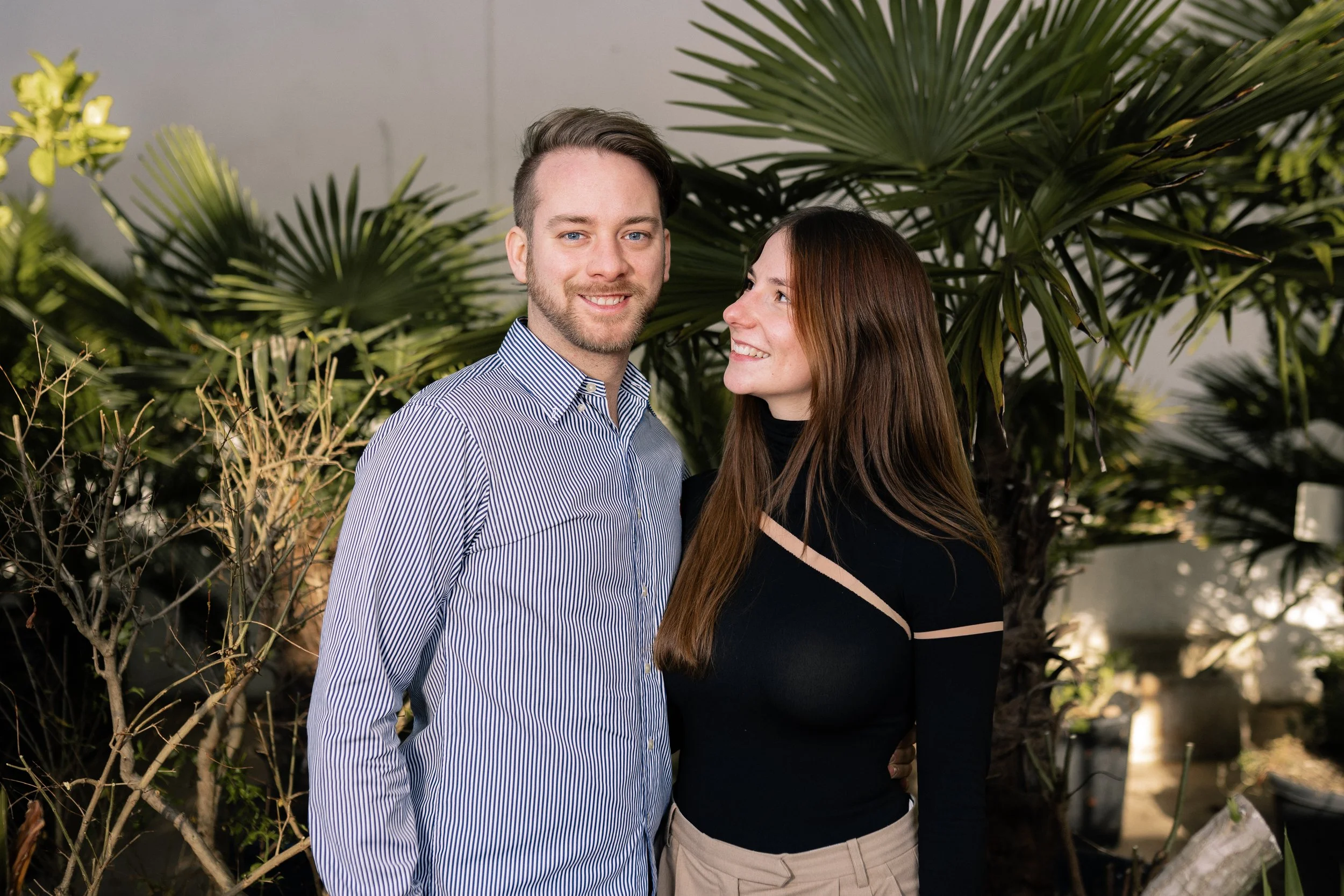 Ein Mann und eine Frau stehen vor einer großen Pflanze und lachen sich an.
