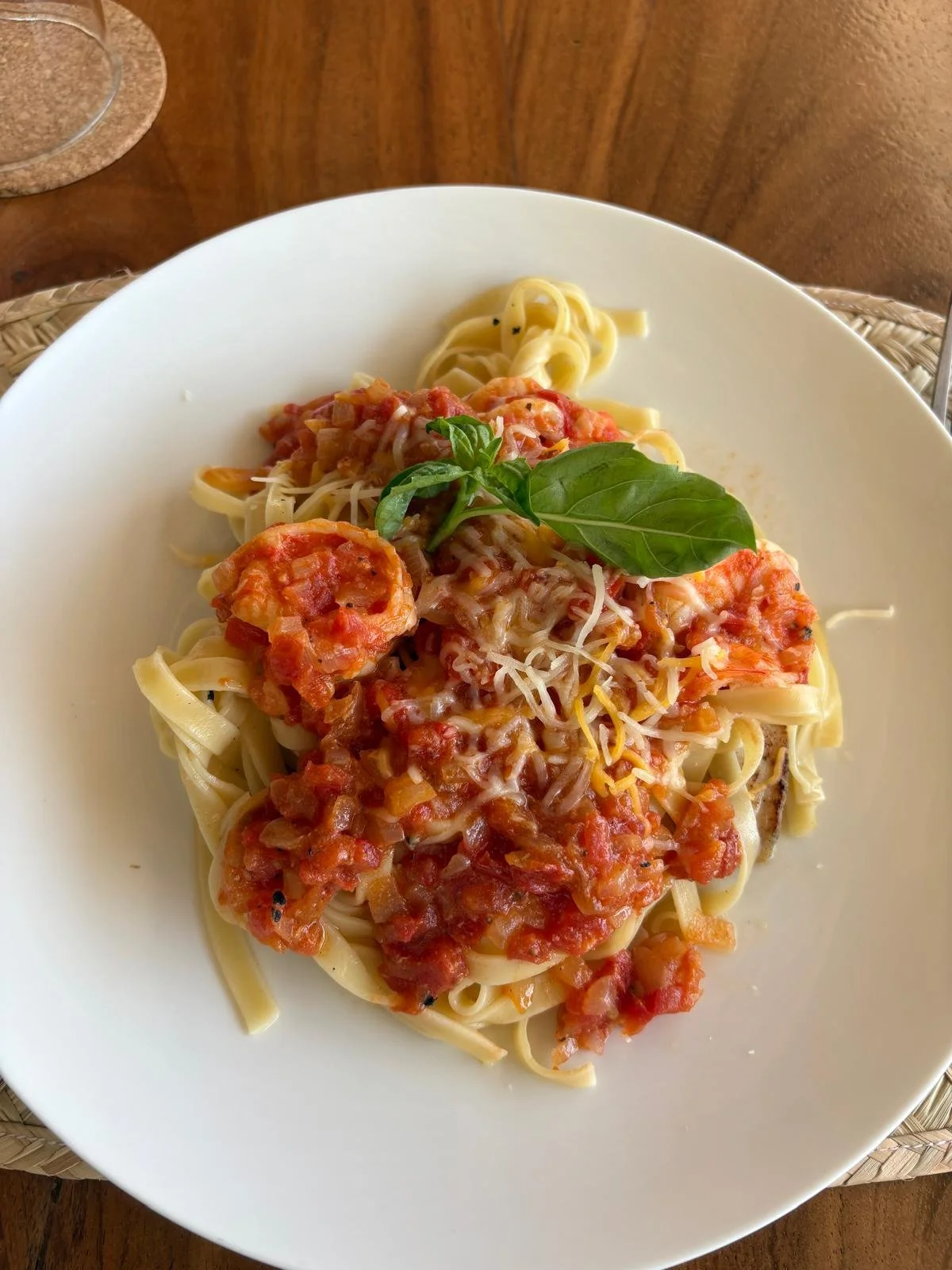 Plate of pasta with tomato sauce, grated cheese, and basil garnish on a white plate, on a wooden table.