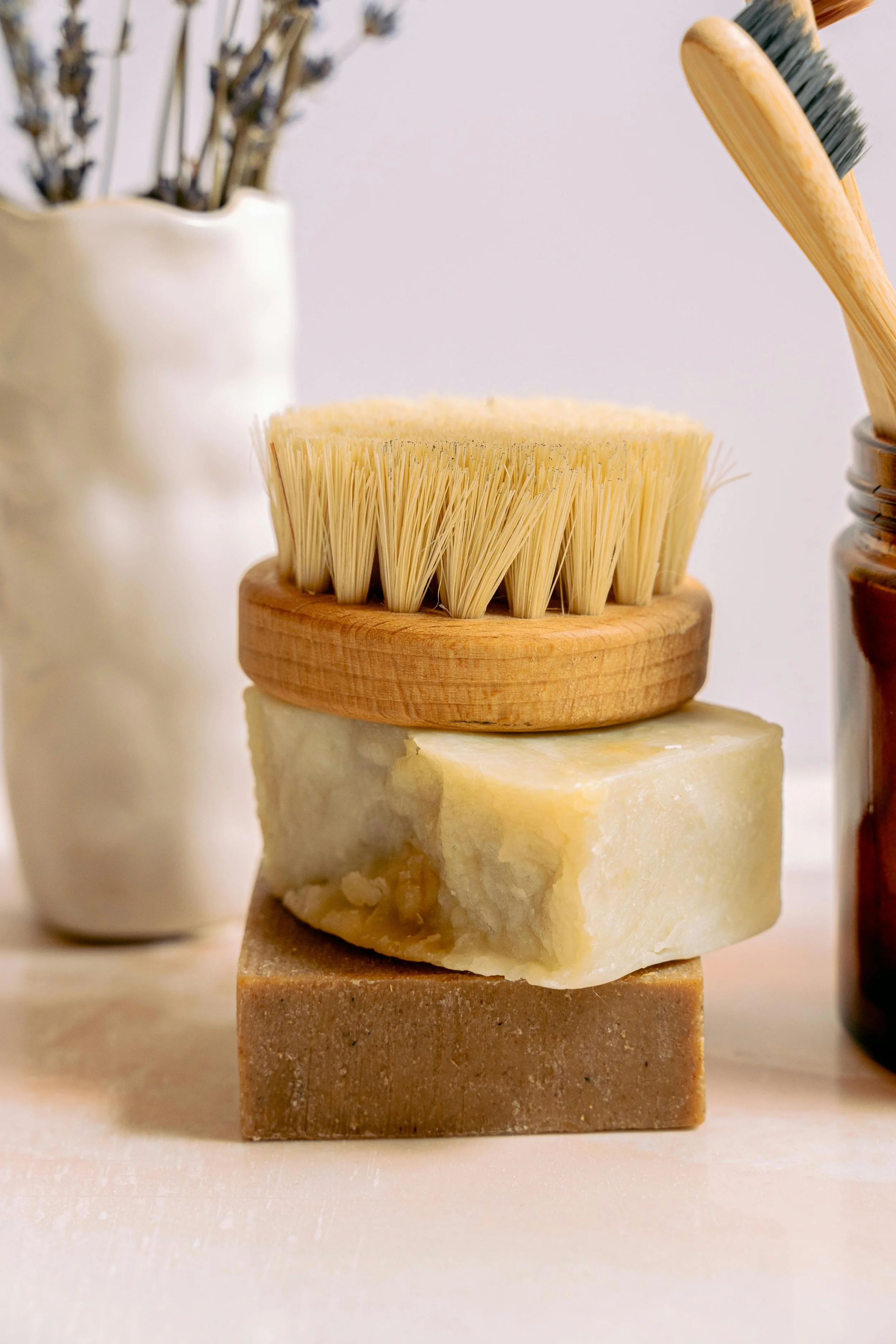 Stack of three natural soap bars with a scrubbing brush on top, surrounded by jars of cleaning tools.