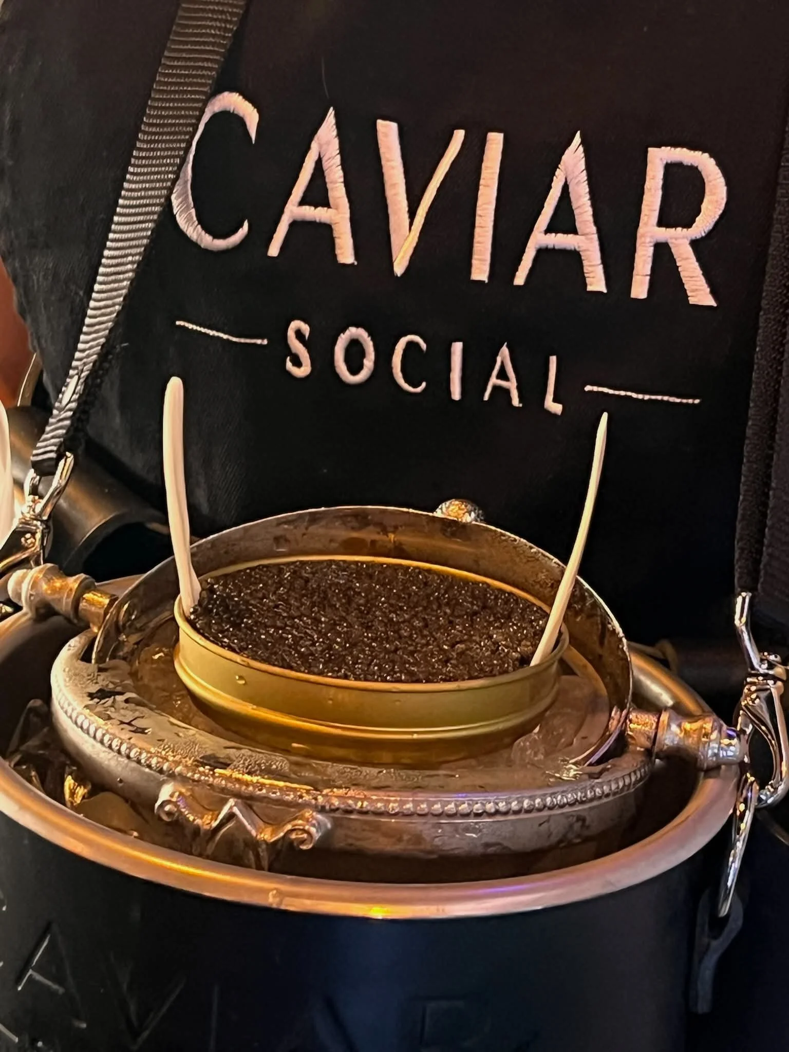 Close-up of a black embroidered patch that reads 'CAVILAR SOCIAL' in pink thread, attached to a black fabric item.