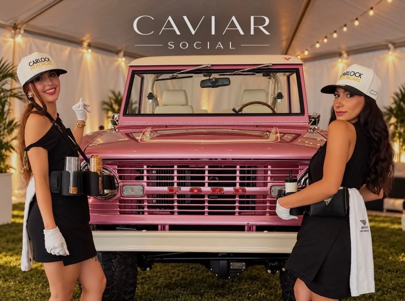 Two women dressed as servers stand in front of a pink vintage Ford vehicle at a social event. The women are wearing black dresses, white gloves, and white caps, with drinks and accessories visible on their belts. The background features a tent with string lights and plants, and the word 'CAVIAR' is displayed at the top.