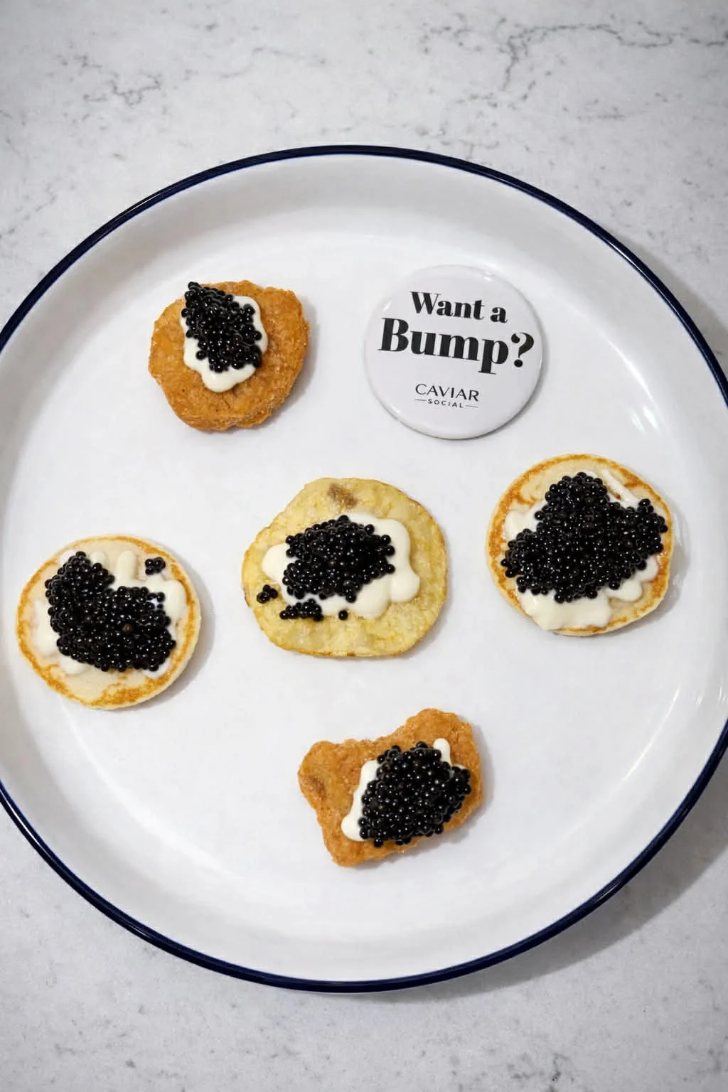 Plate with five canapés topped with caviar and cream, and a small round button displaying text 'Want a Bump?' from Caviar Social.