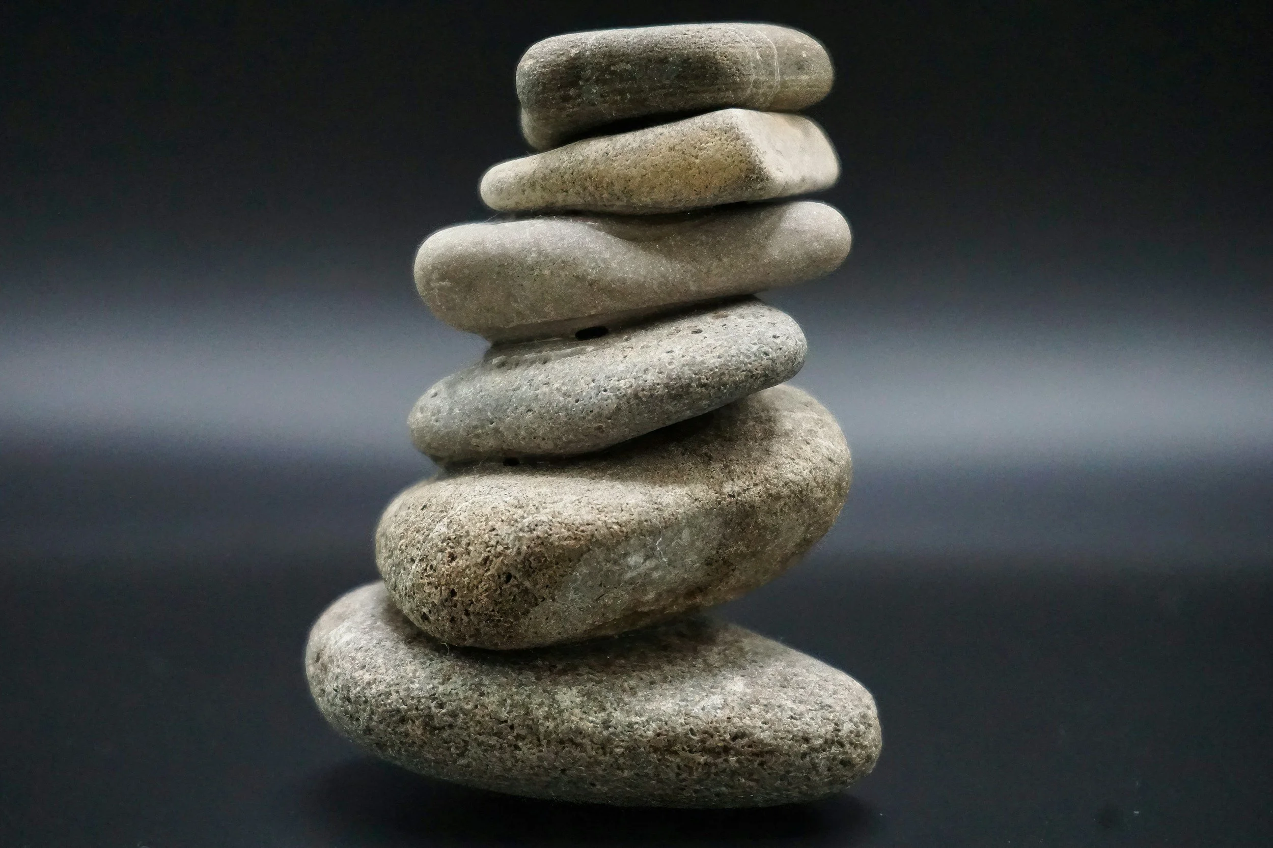 A vertical stack of seven smooth, rounded stones of varied sizes and colors, arranged on a dark background.