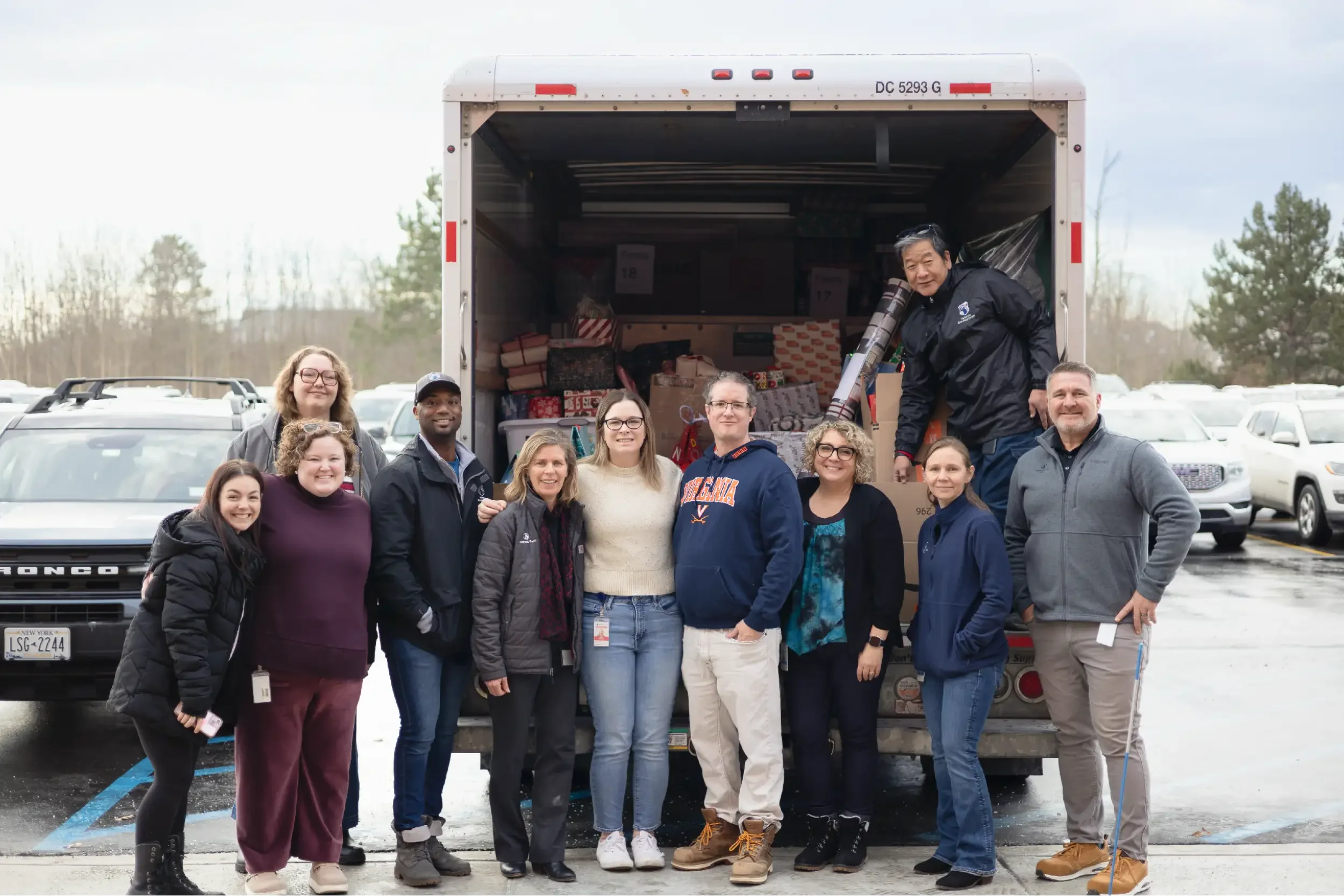 Group of people standing in front of a truck filled with holiday gifts in a parking lot.