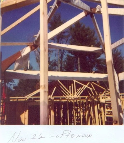 Construction site with wooden framework for a building, with trees and a blue sky in the background.