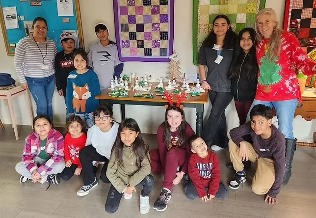 Group of children and adults with holiday-themed decorations and quilt displays in the background.