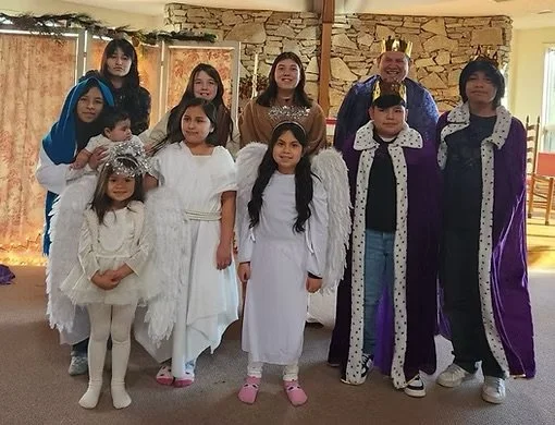 A group of children dressed as angels and kings for a Christmas play inside a room with stone walls and wooden furniture.