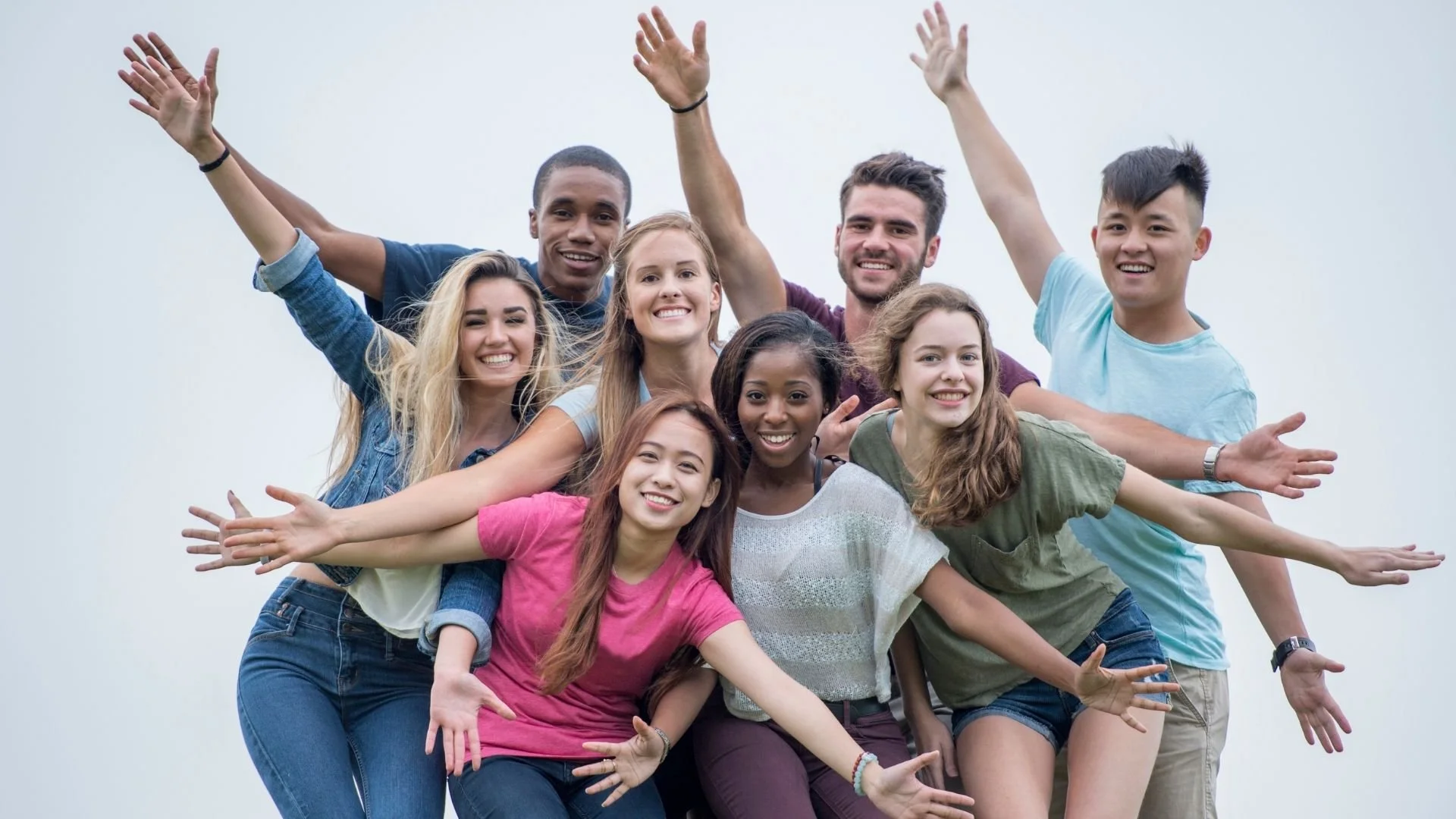 Group of diverse young adults smiling and having fun outdoors against a plain sky background.